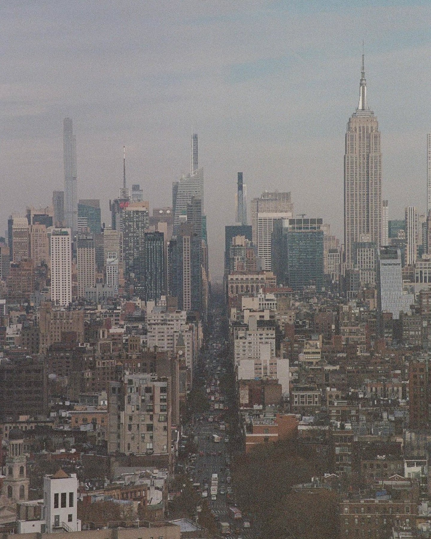 A city skyline featuring numerous high-rise buildings, including the Empire State Building, seen through a hazy atmosphere.