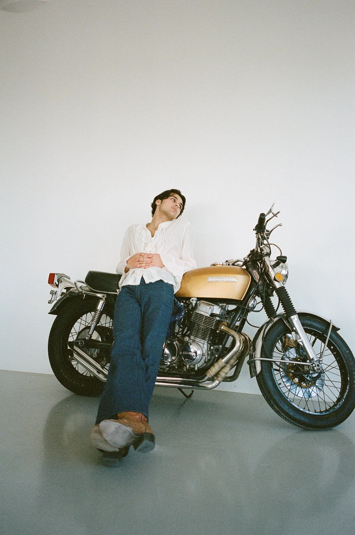 A woman leaning against a vintage Honda motorcycle in a plain white room.