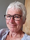 A portrait of a woman with short white hair and glasses, smiling at the camera.