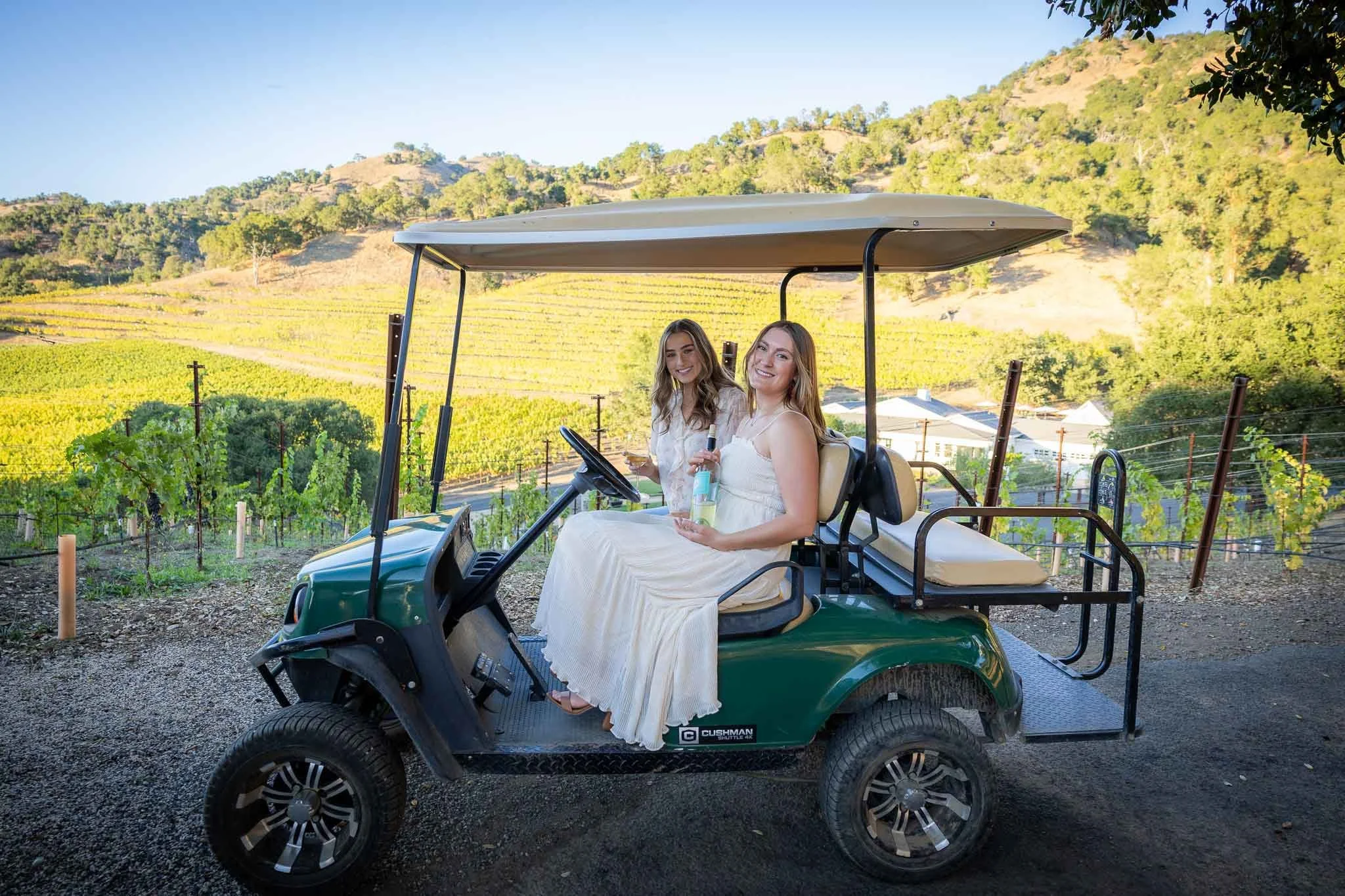 two women from EveryGAL seated on a golf cart overlooking the vines