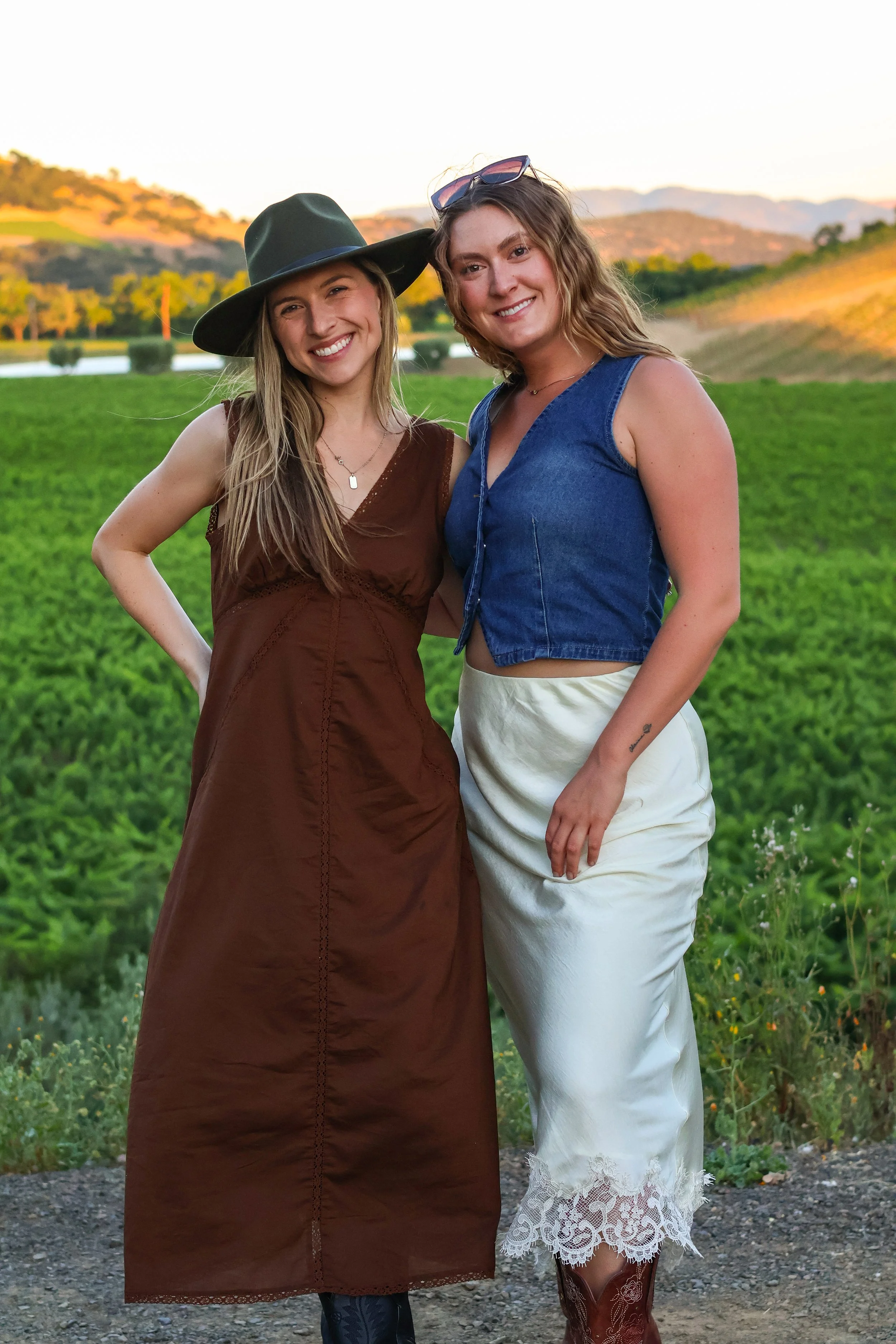 Managers Kate and Julia stand together at their family property, Ilsley Vineyards, during sunset, smiling at the camera during a wine club event.