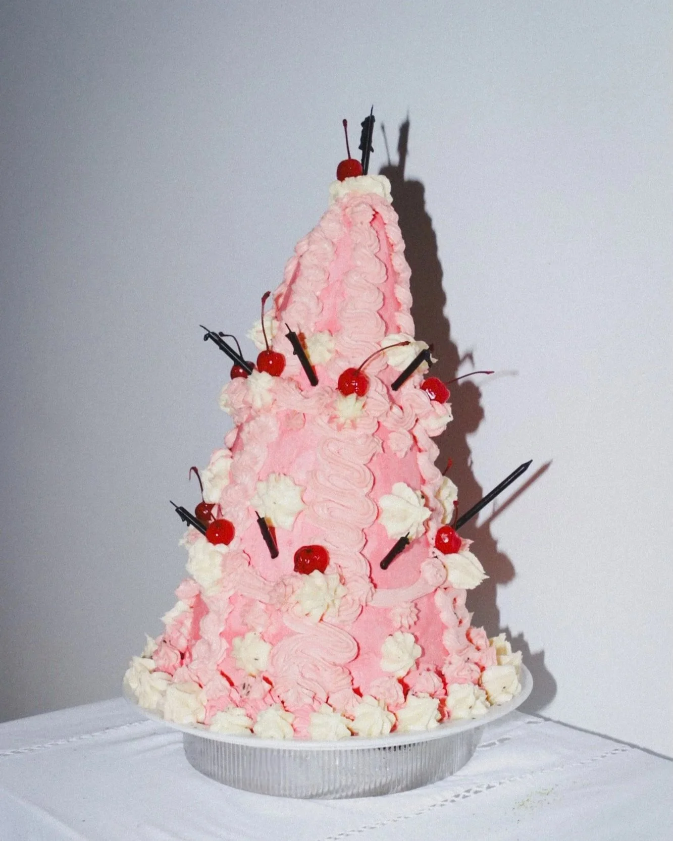 Cake shaped like a pink Christmas tree decorated with cherries, whipped cream, and chocolate sticks.