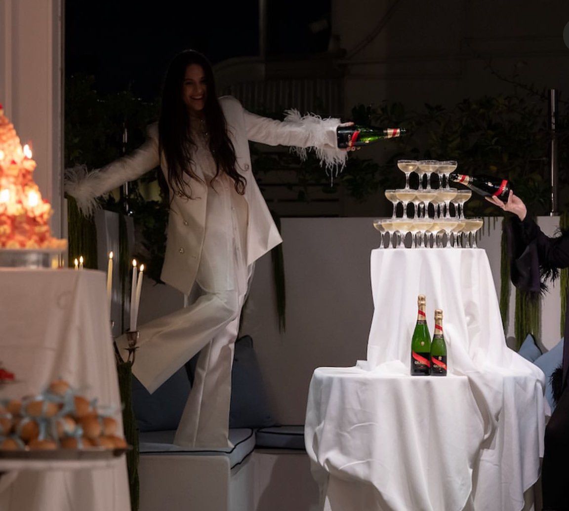 Woman in white suit celebrating with champagne at a party