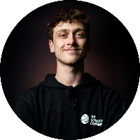 Young man with curly hair smiling, wearing a black hoodie with a logo, against a dark background.