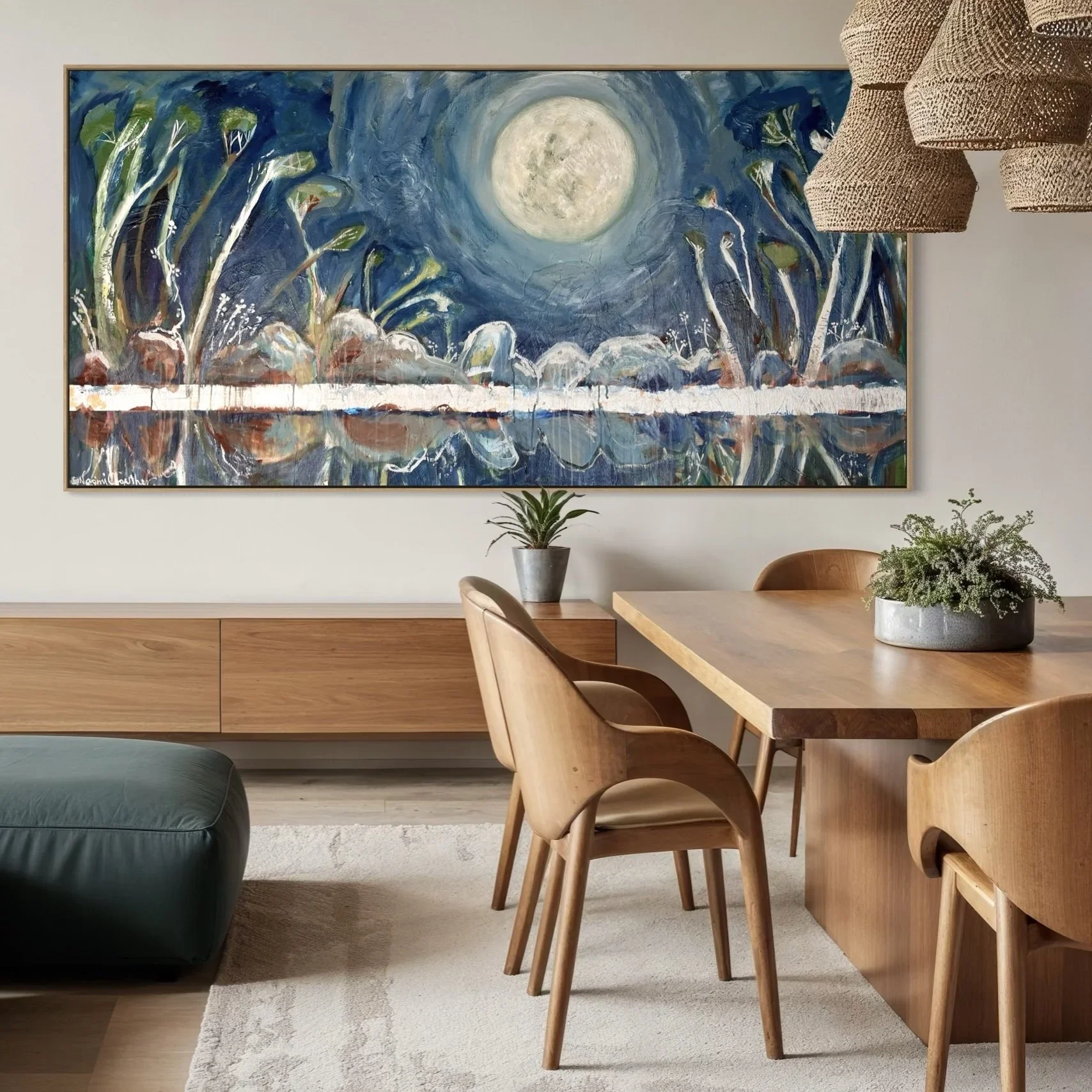 A modern dining room with a wooden table and chairs, a large abstract painting of a full moon over a blue landscape, and potted plants.