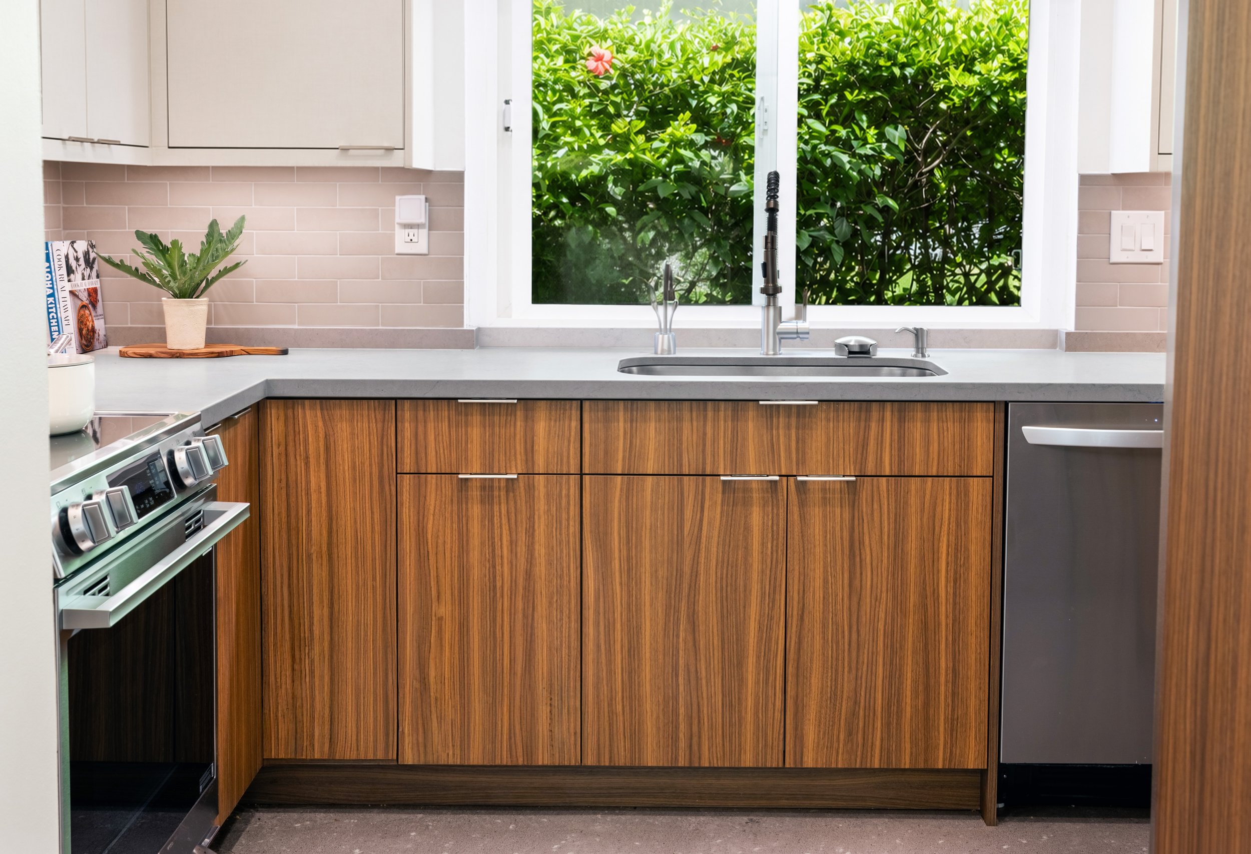 Bright kitchen sink area with a large picture window, custom cabinetry, quartz countertops, and views of tropical greenery.