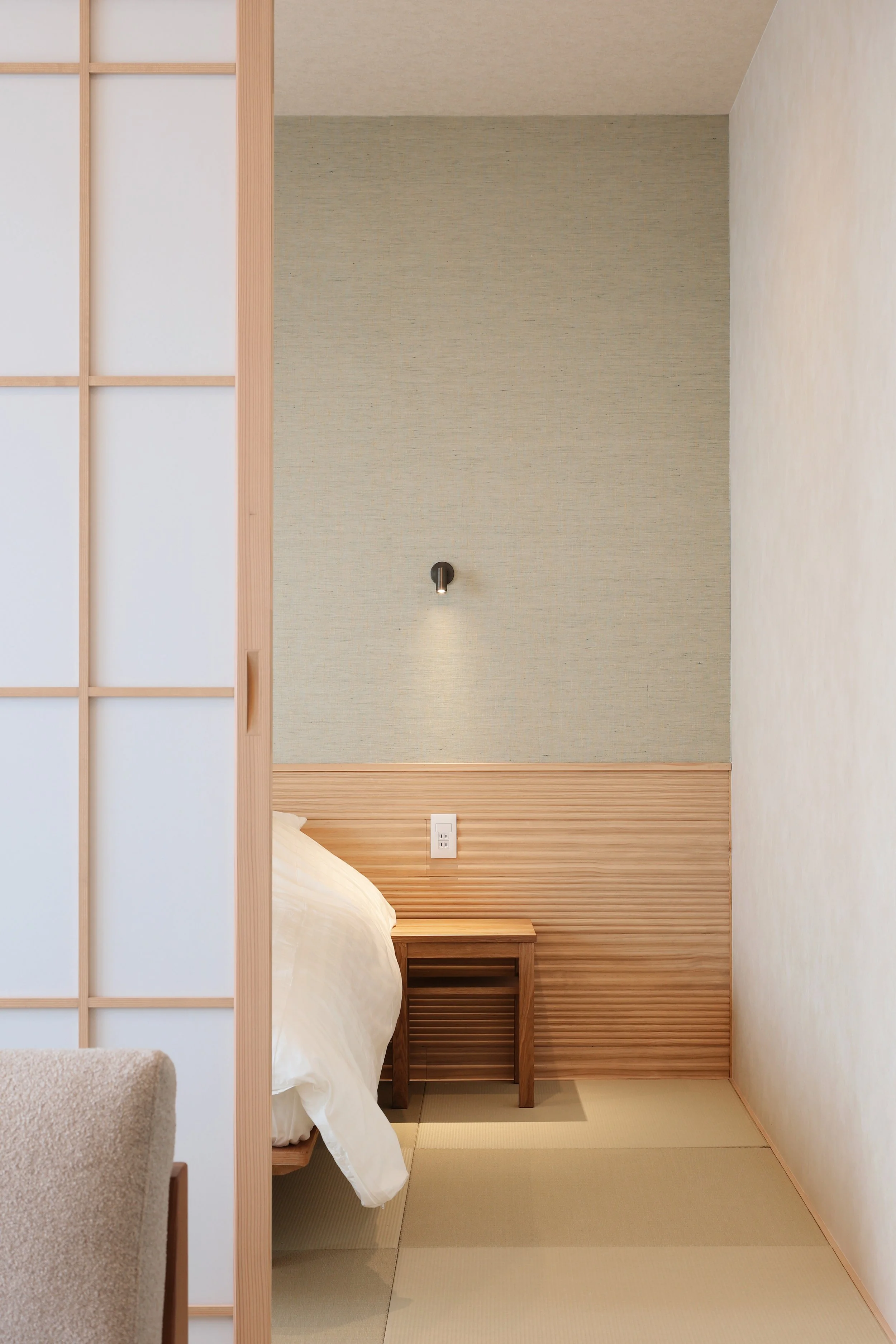 A minimalist Japanese-style bedroom with sliding shoji door, tatami mats, and a small wooden bedside table.