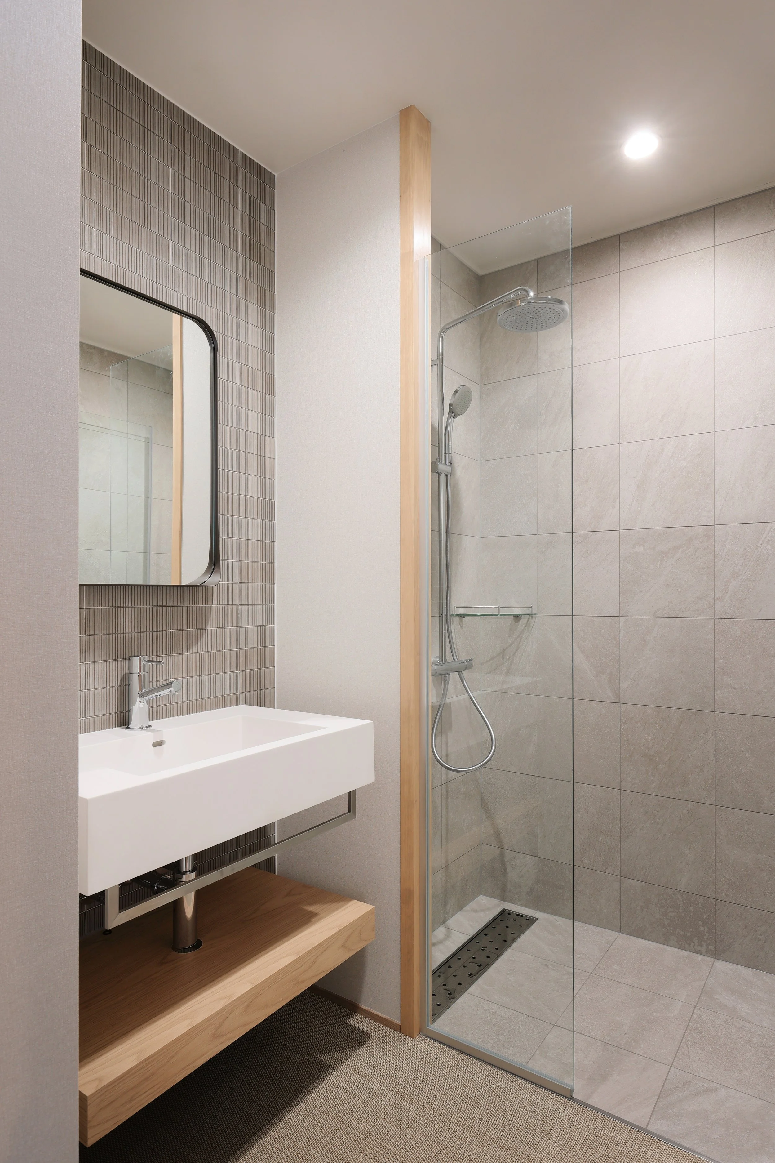 Modern bathroom with a wall-mounted white sink, a rectangular mirror, and a walk-in shower with a glass door, beige tiled walls, and a rain showerhead.