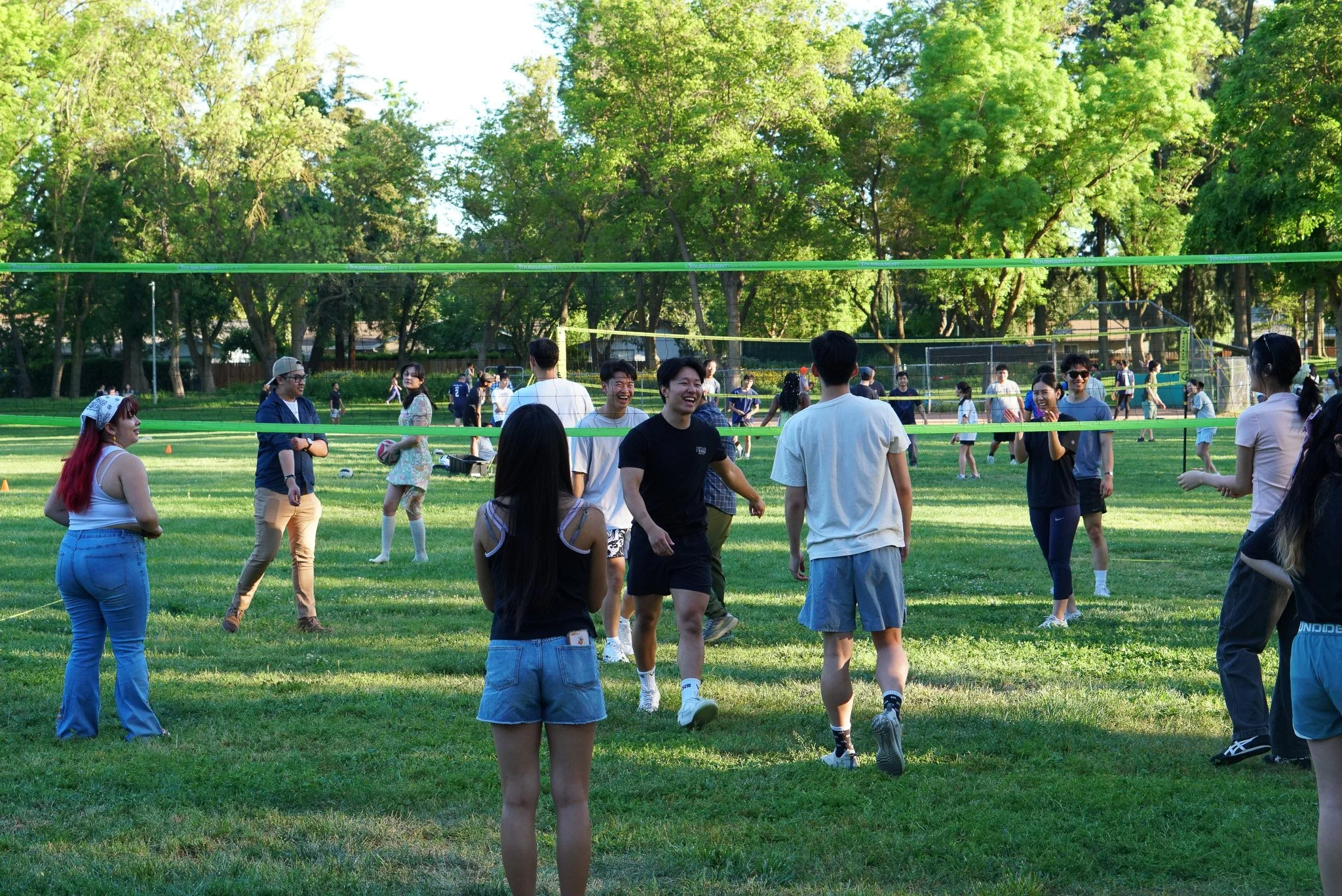 a group of UC Davis playing a volleyball game in a park with tall green trees in the background after Easter Sunday Service. 