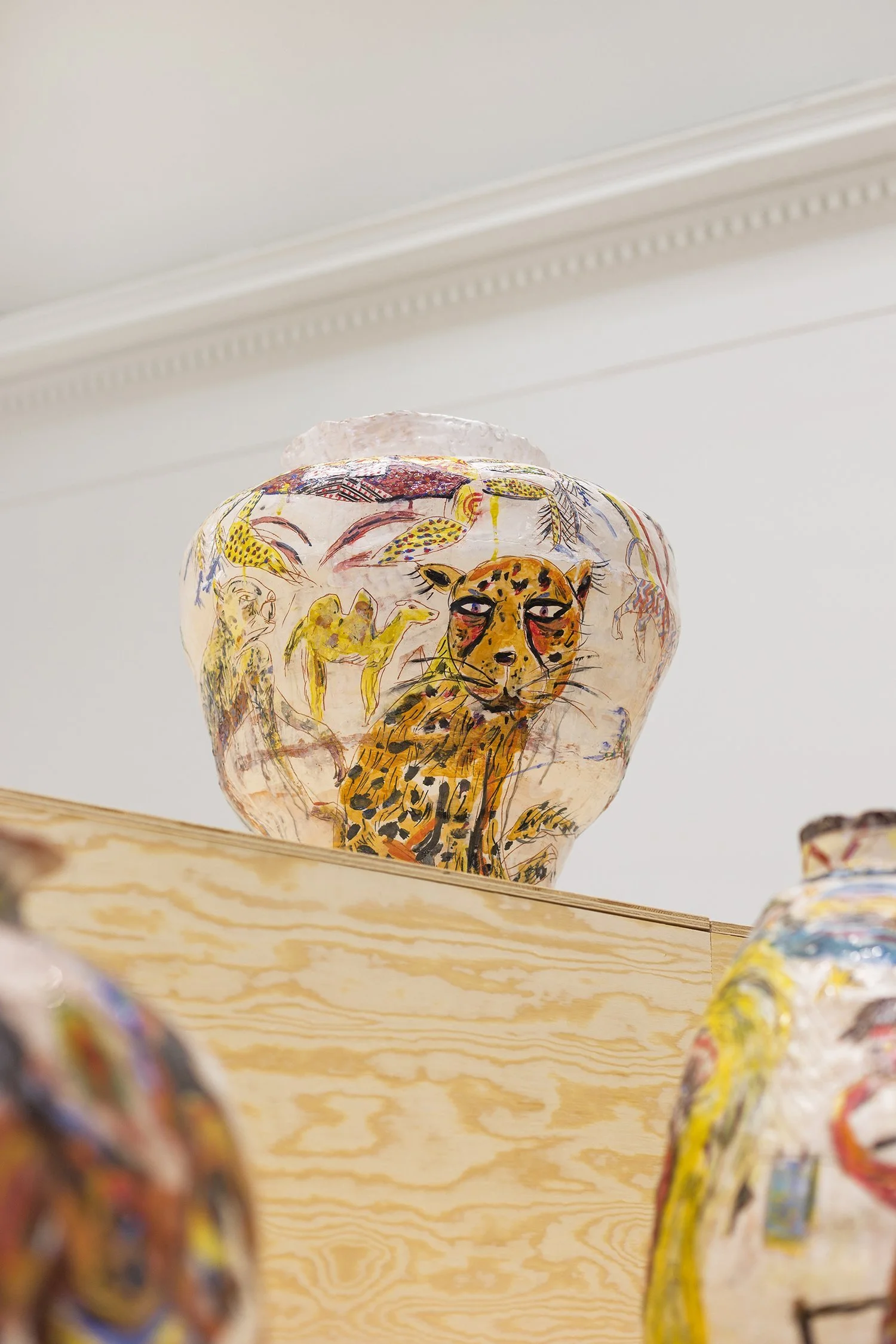 Decorative glass vase with painted animal drawings, including a leopard, camel, and various abstract designs, placed on a wooden shelf.