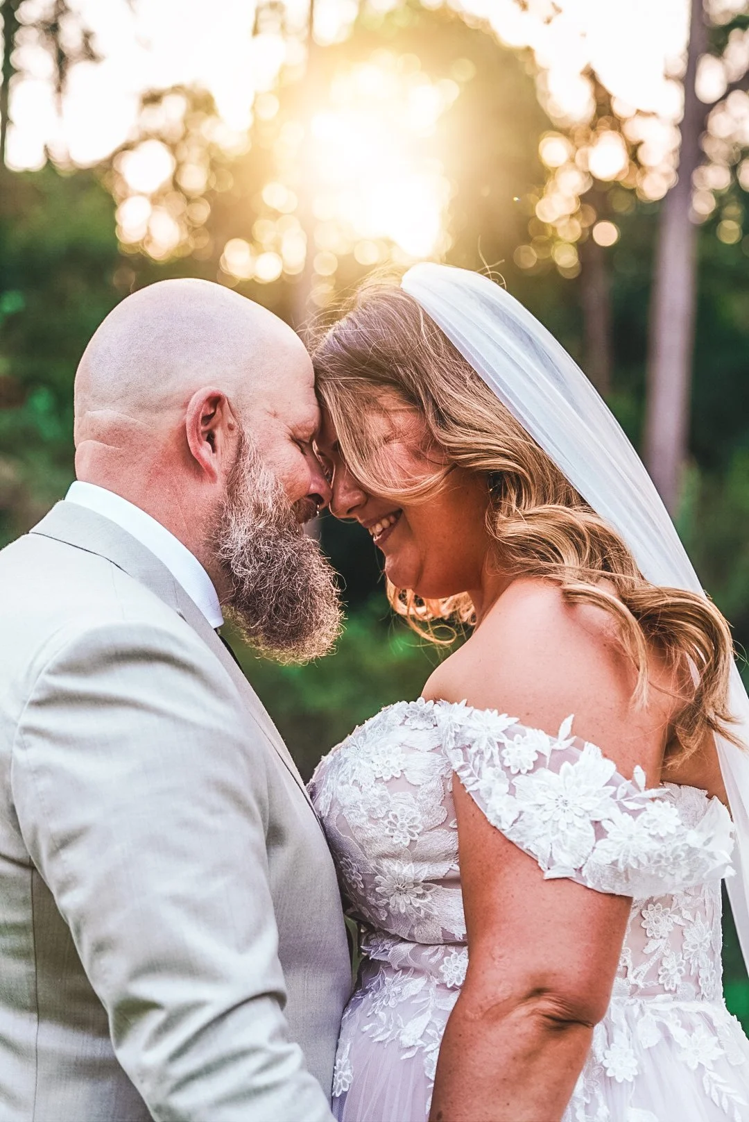 A bride and groom outside at sunset touching foreheads and smiling.
