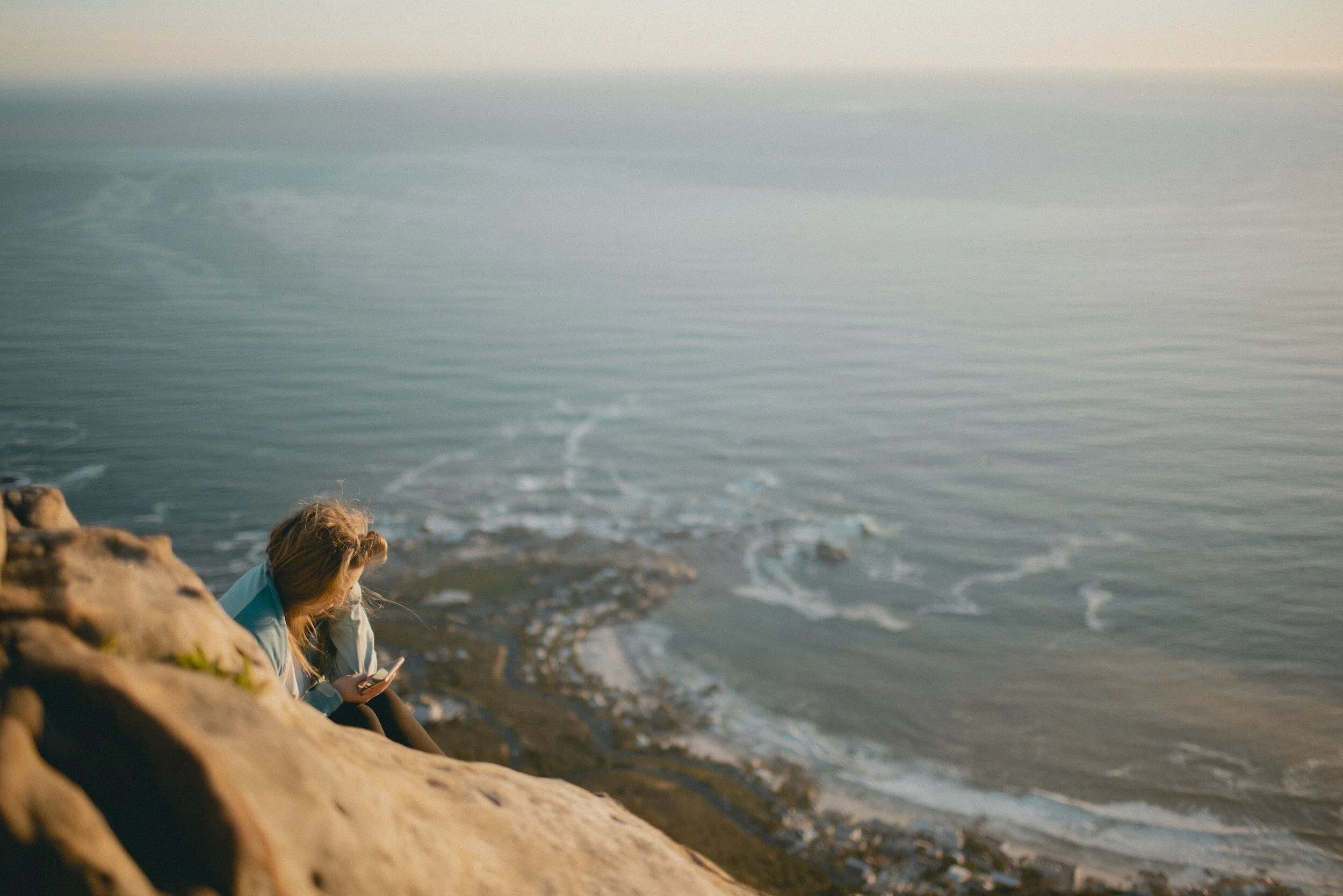 Woman sitting of rock above the sea, checking her phone