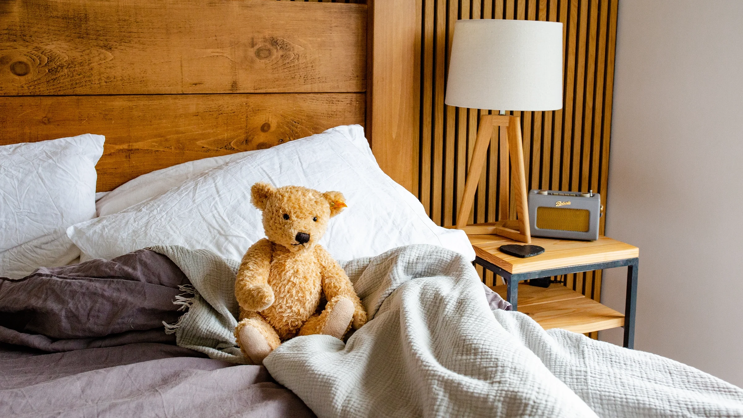 Bedroom interior with a wooden headboard, coral bedding, a teddy bear, table lamp, and retro radio on a nightstand.