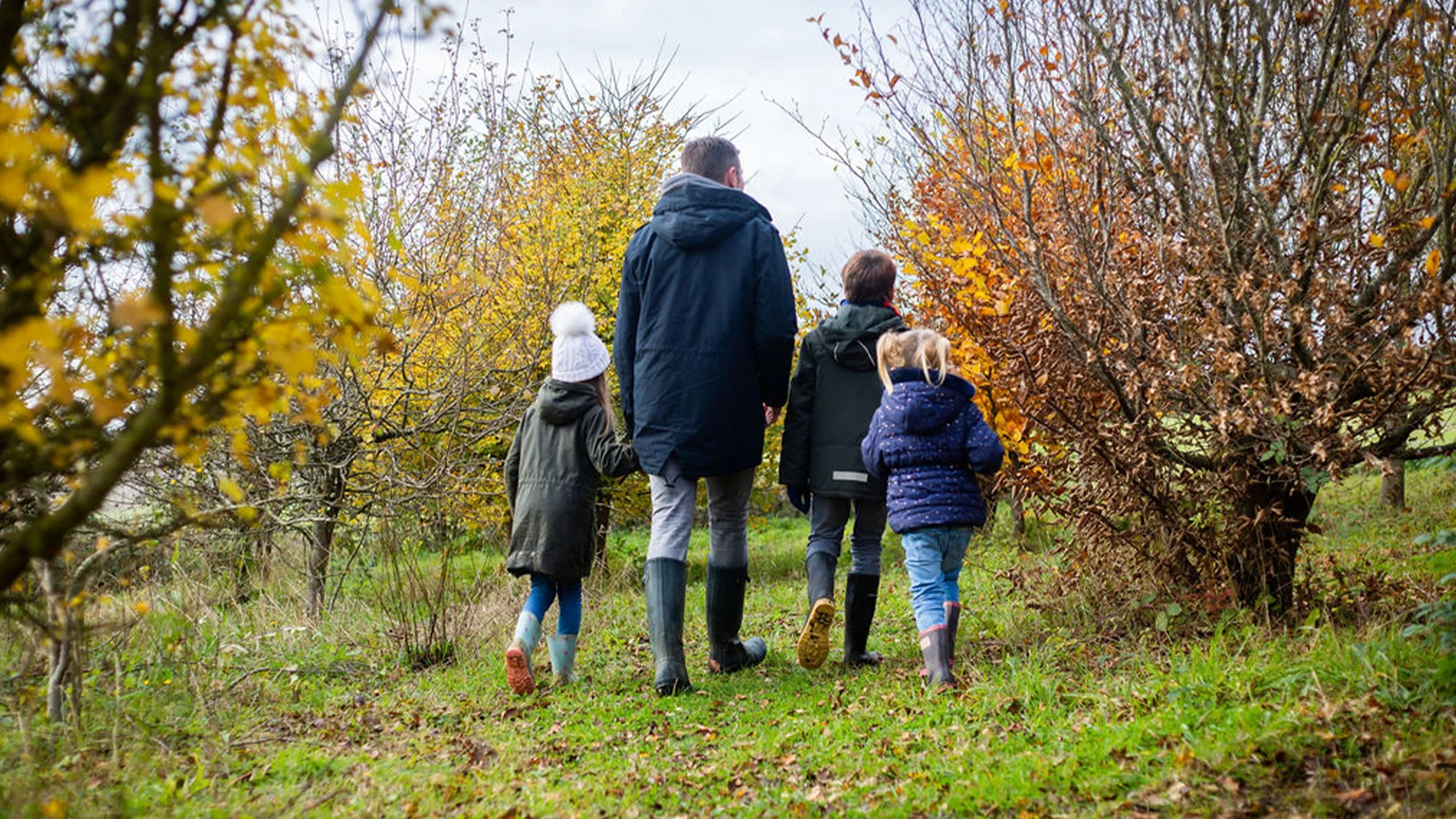 Father and daughter walking on a grassy path in a green hilly landscape.