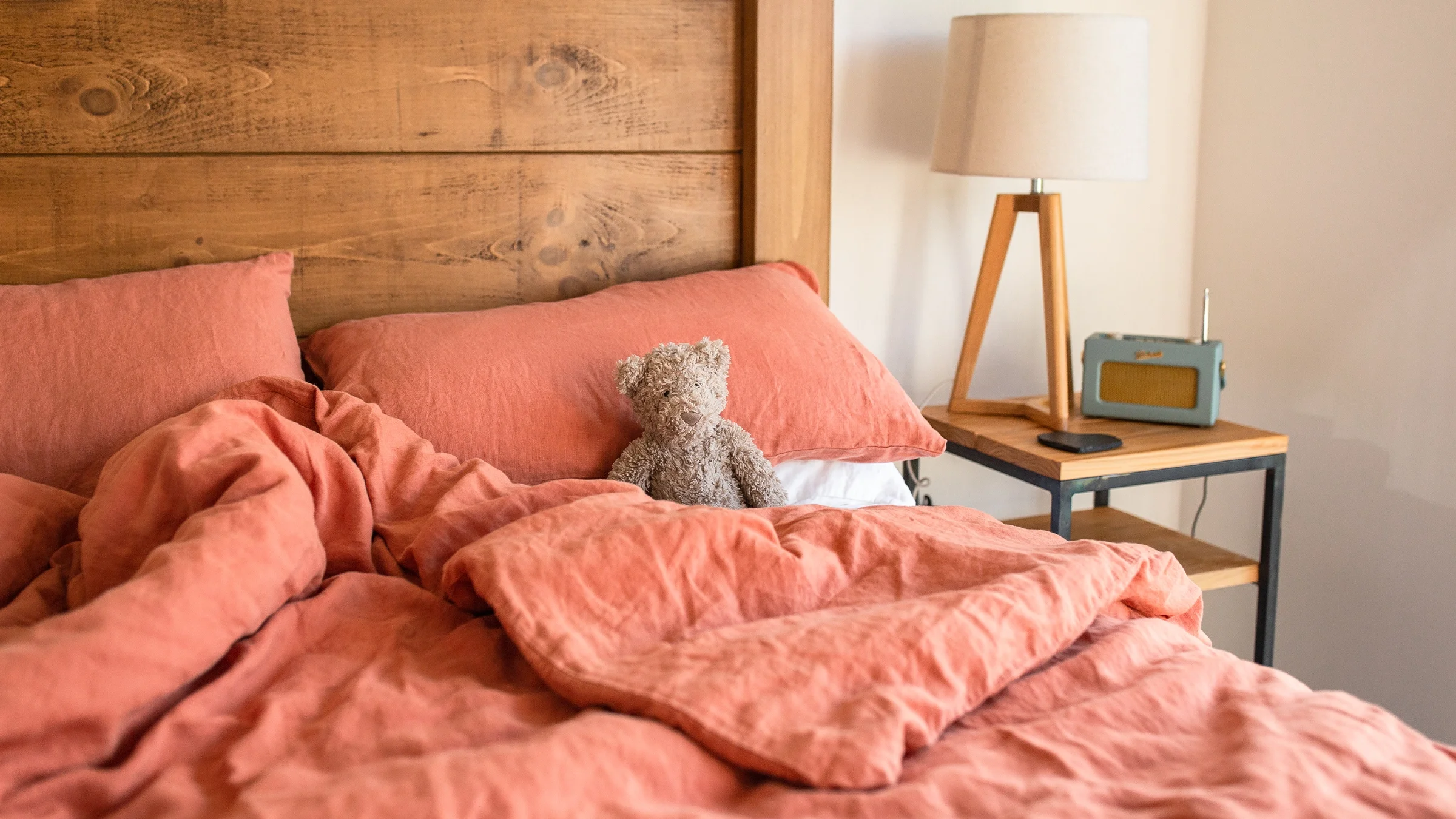 Bedroom with wooden bedframe, pink bedspread, pillows, bedside tables with lamps, and large window overlooking garden.