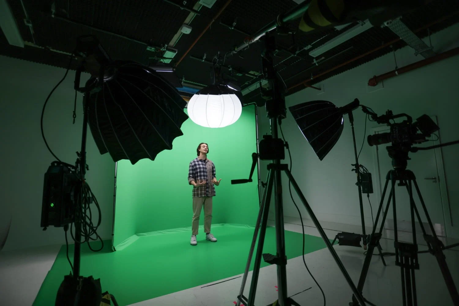 Person stands on a Green Screen Studio set, surrounded by cameras and lighting equipment in a professional film studio.