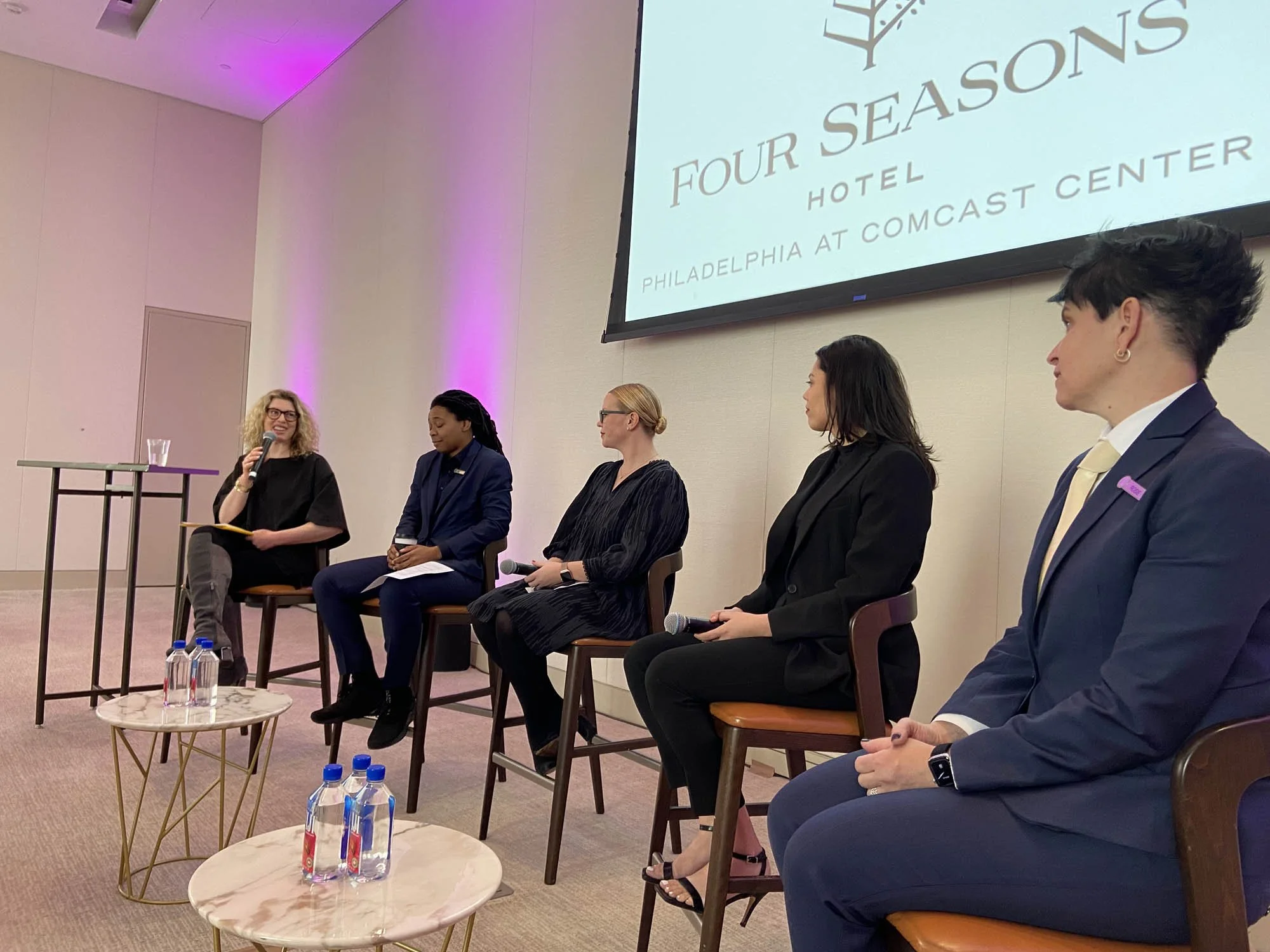 A panel of five women seated on stage at a conference, with a large screen behind them displaying the Four Seasons Hotel Philadelphia logo.