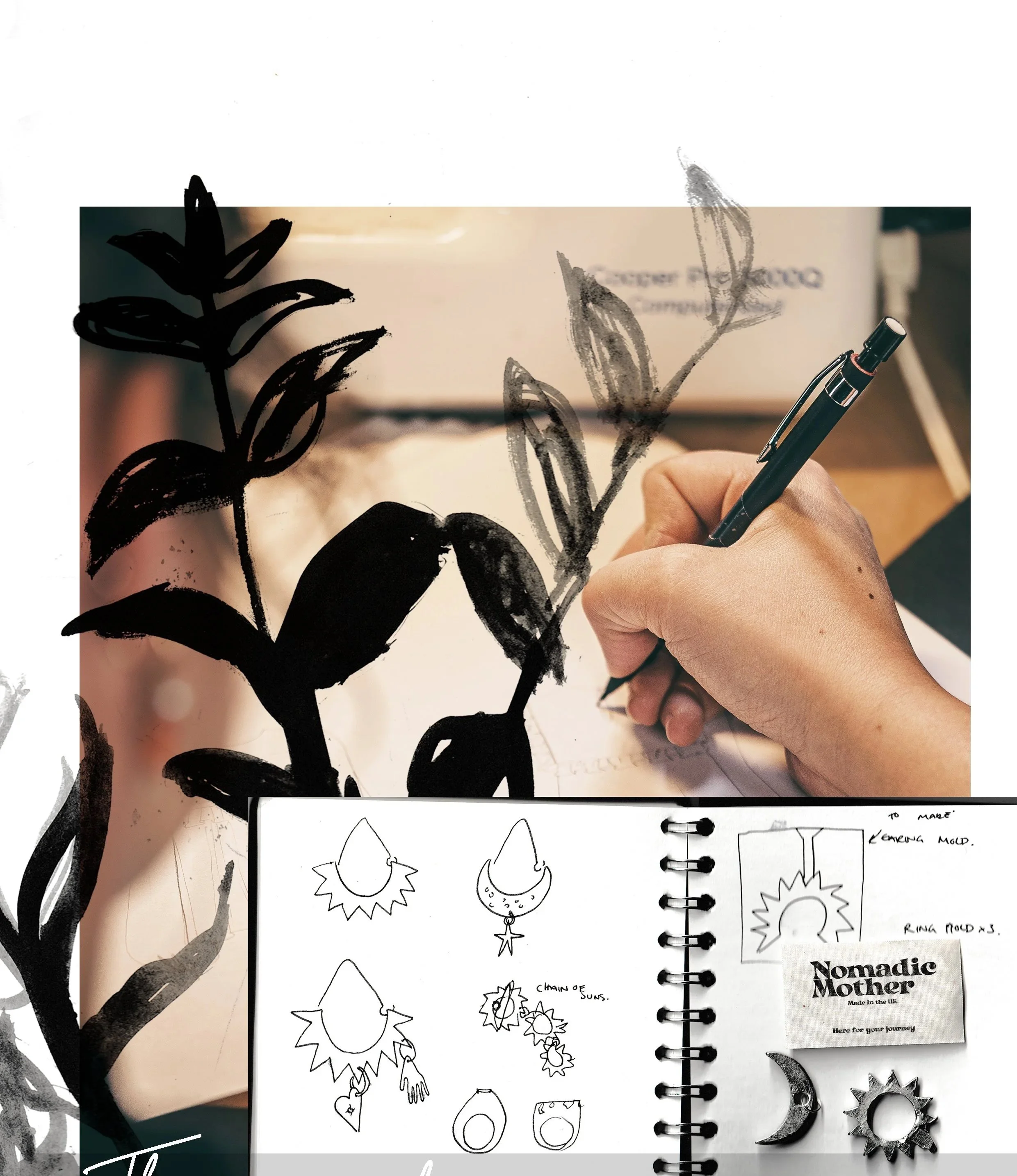 A person is drawing large black and gray botanical sketches on a white paper with a black pen. Below, in a spiral notebook, there are small sketches of jewelry designs, including moon and sun motifs, hanging ornaments, and circular elements. There are also printed notes and a business card labeled 'Nomadic Mother.'