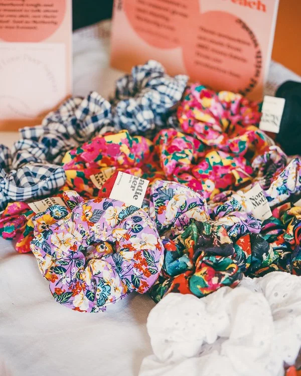 A variety of colorful fabric scrunchies with floral and checkered patterns displayed on a white surface.