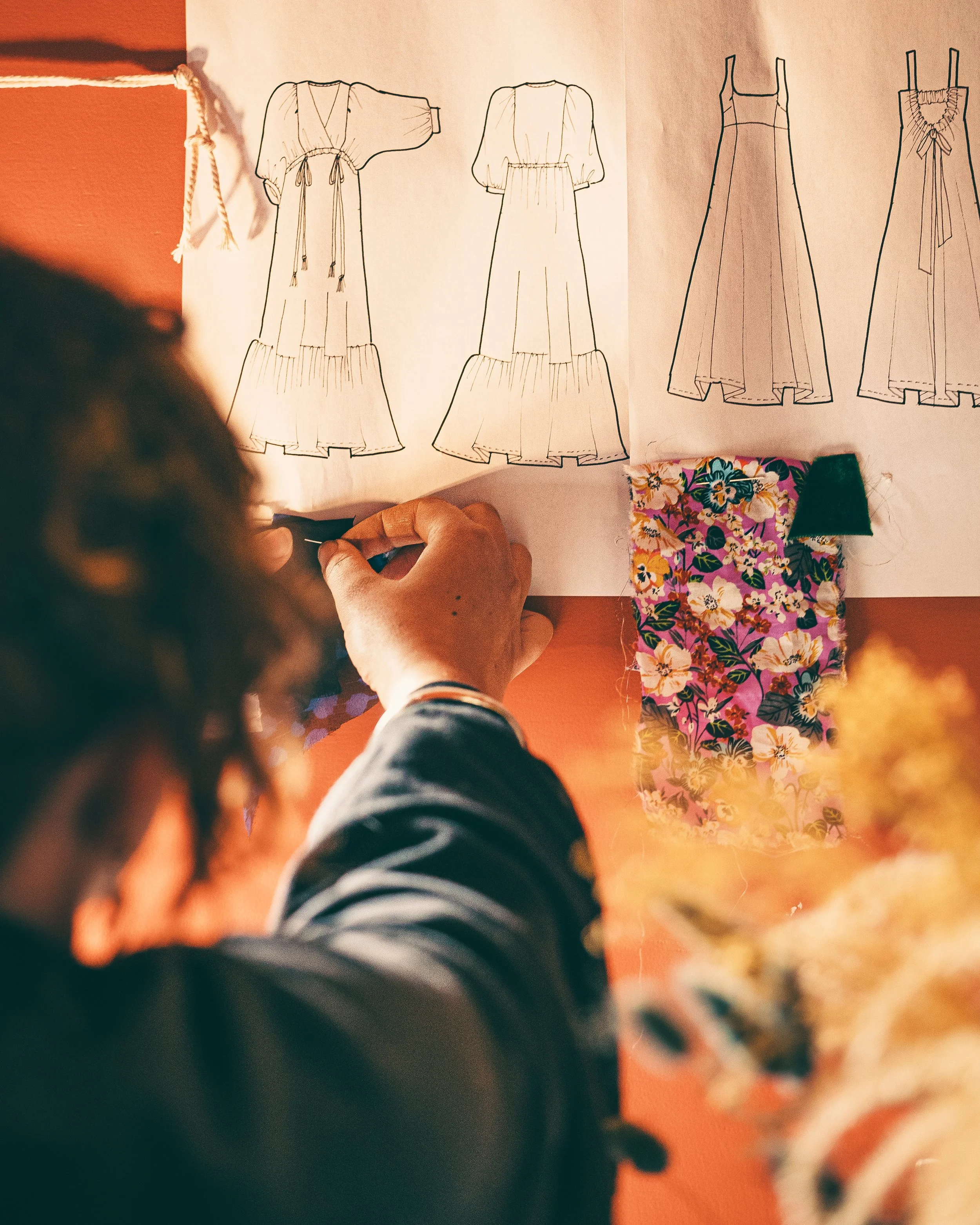 Person working on fashion sketches for dresses, with fabric samples on the table.