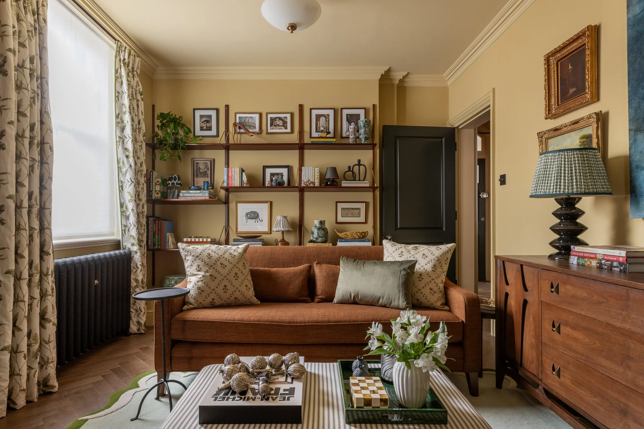 Traditional English style living room in London with a terracotta sofa, bespoke wooden shelving, curated art, and warm lighting in a restored Victorian home.