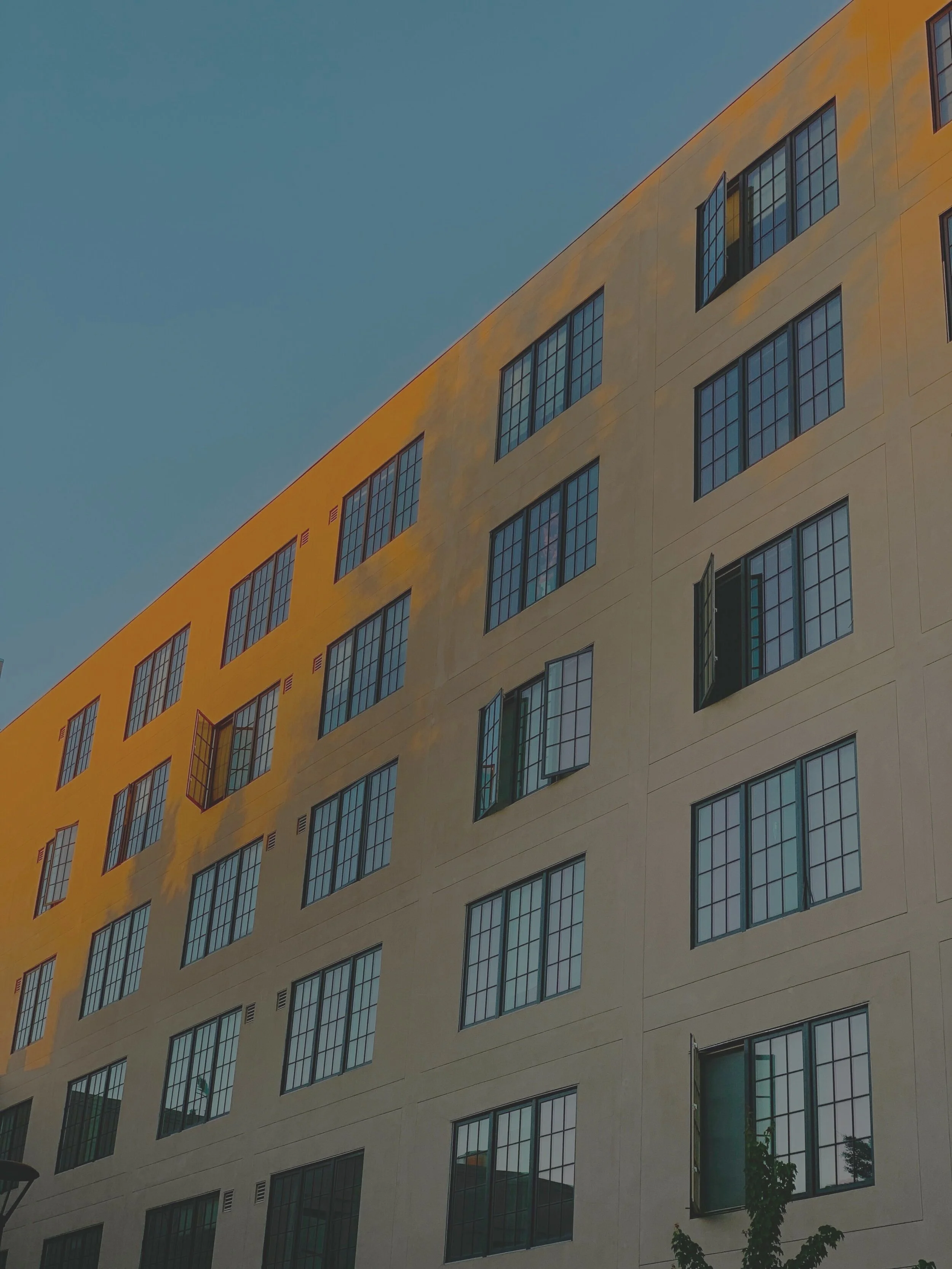 A multi-story building with large windows, some open, against a clear blue sky.