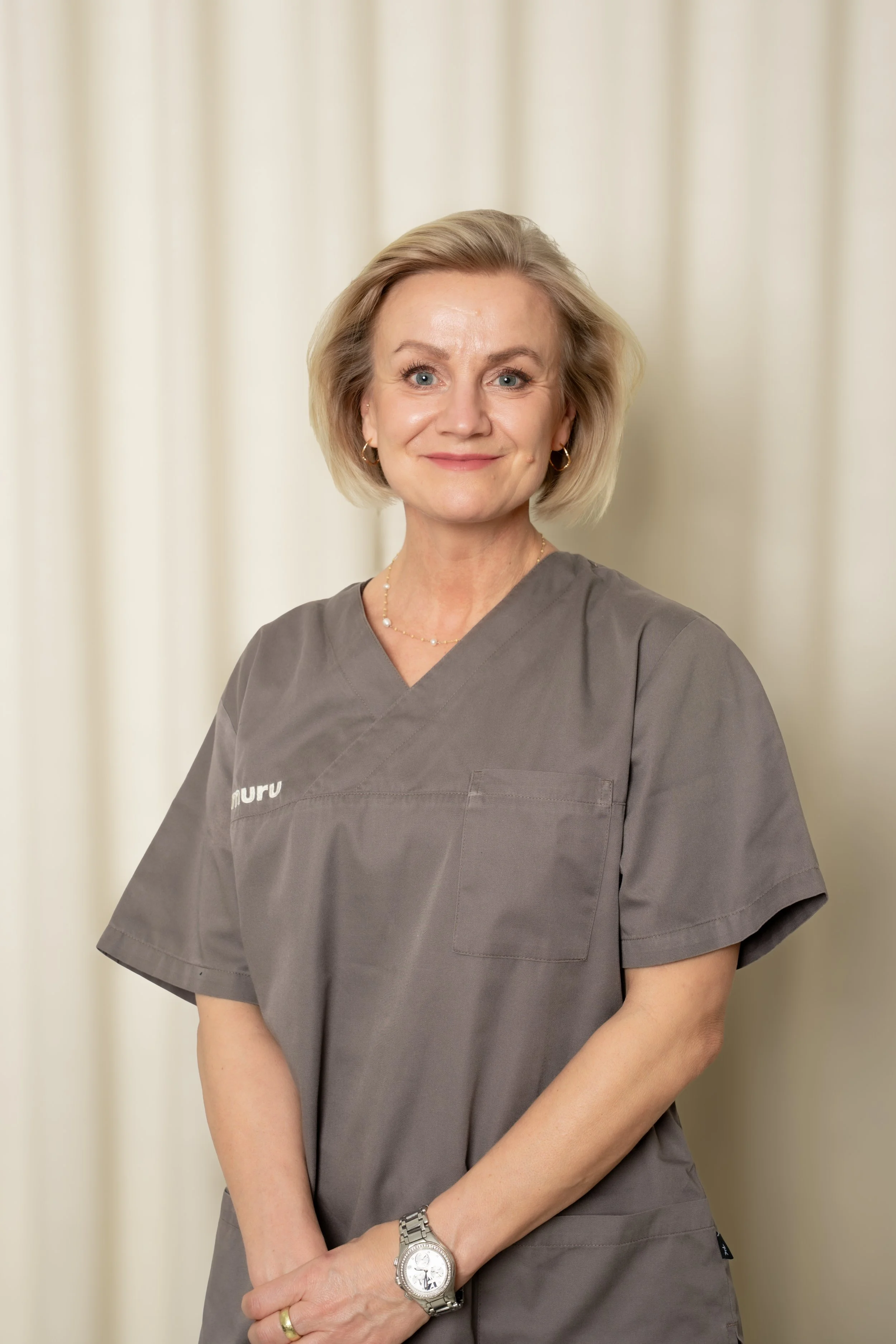 En kvinde iført grå uniform står foran en lys baggrund, smilende.