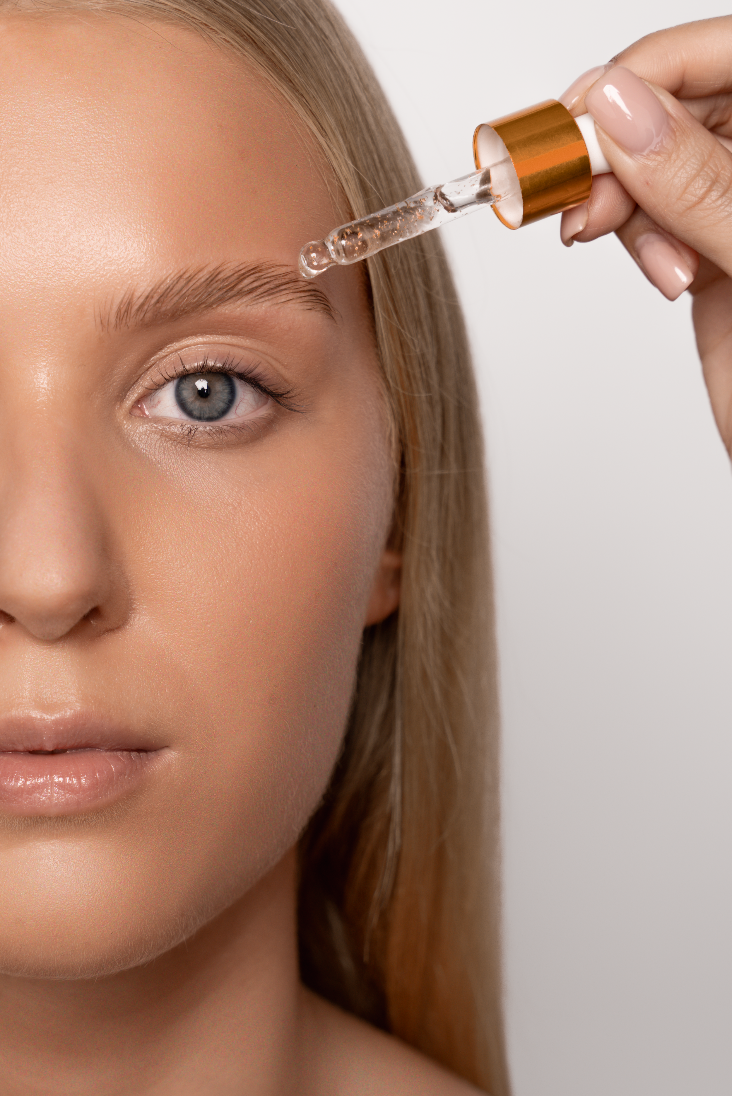 En kvinde med blond hår får påført serum på øjenbryn med en pipette.