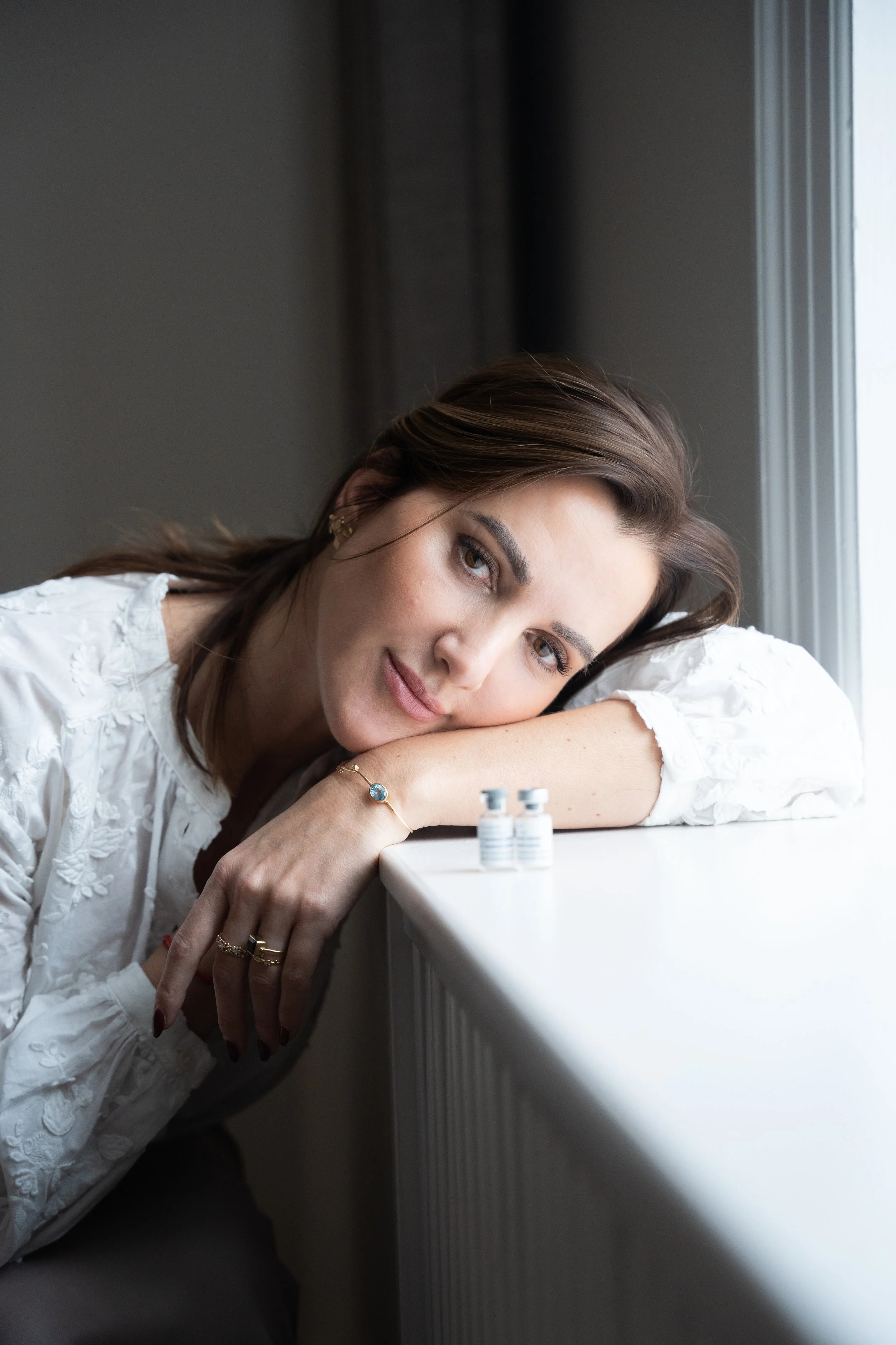 Kvinde hviler sit med hovedet på armen foran en vindue med medicinampuller foran.