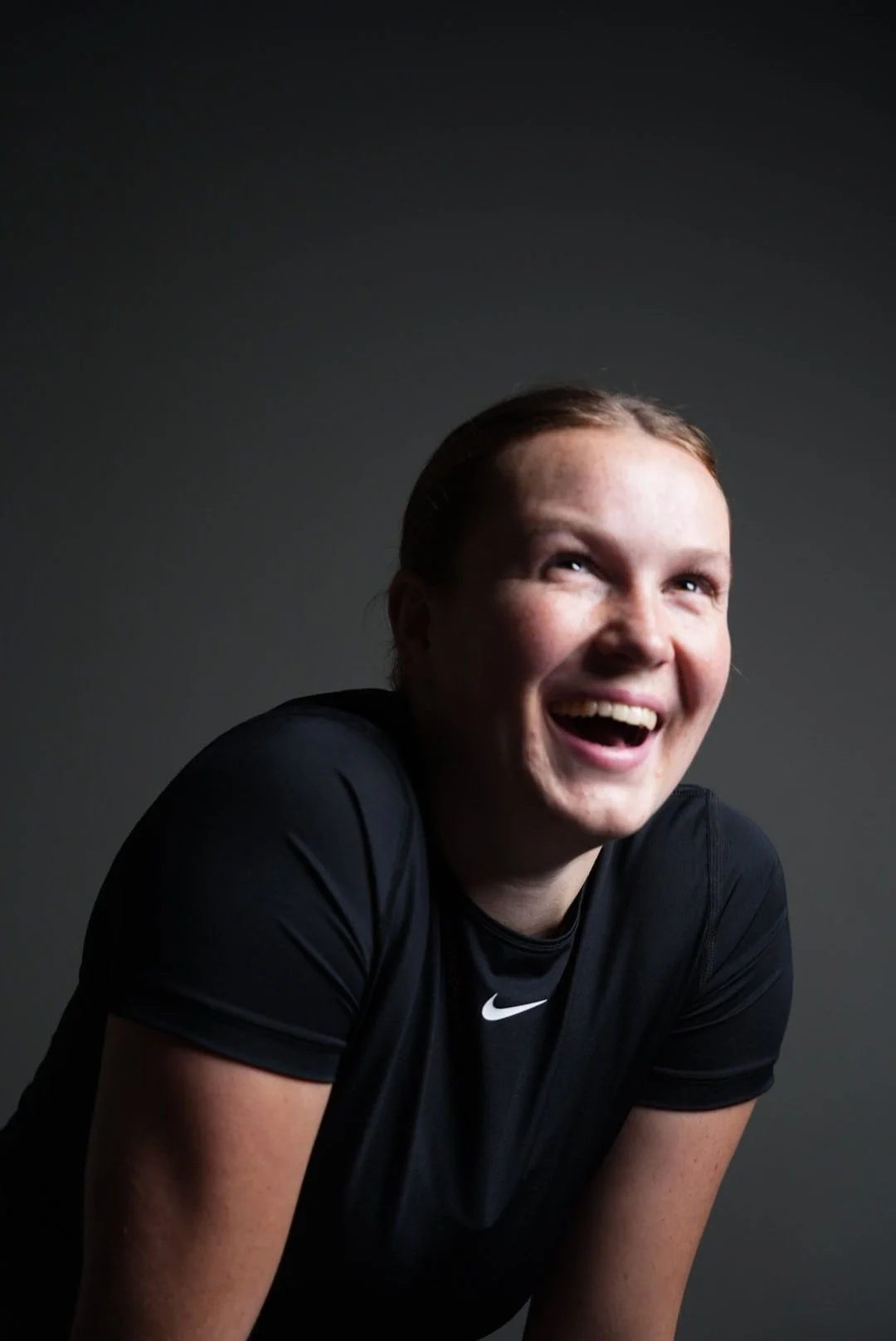 En glad kvindelig atlet i sort Nike-trøje smiler i et studie med mørk baggrund.