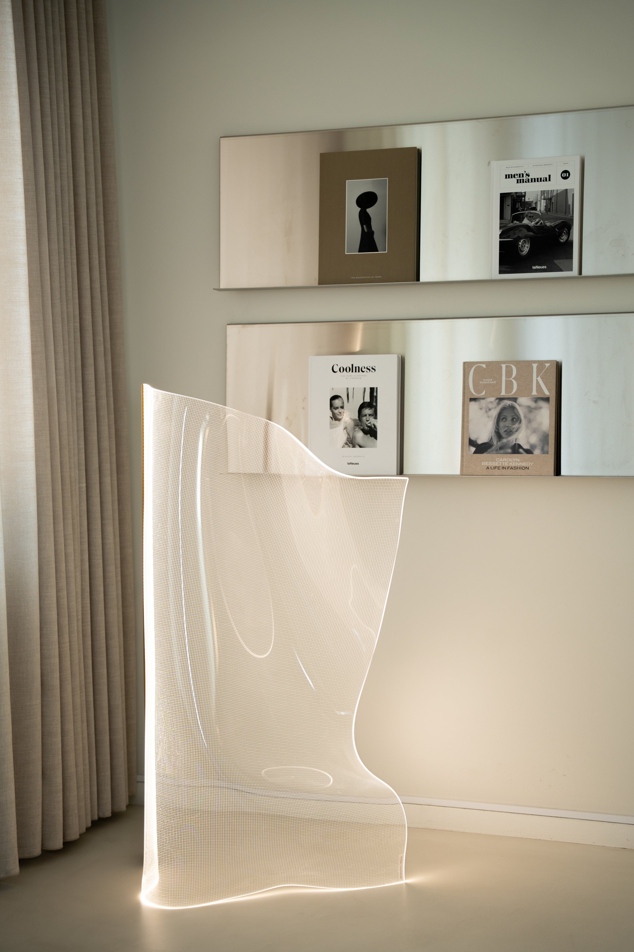 En moderne, kurvet, lysekrone-lignende lampe i hvid, placeret i et rum med bøger på væggen.