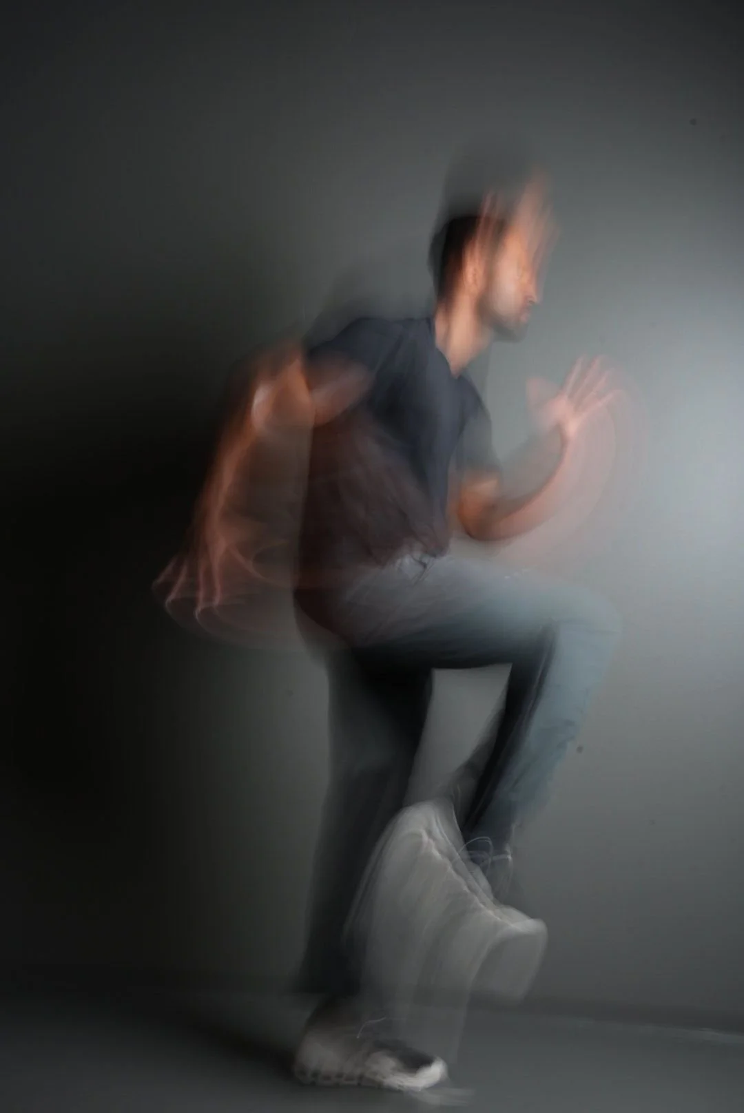 Person i bevægelse, træner eller løber, med uskarphed og sløring, mod en neutral grå baggrund.
