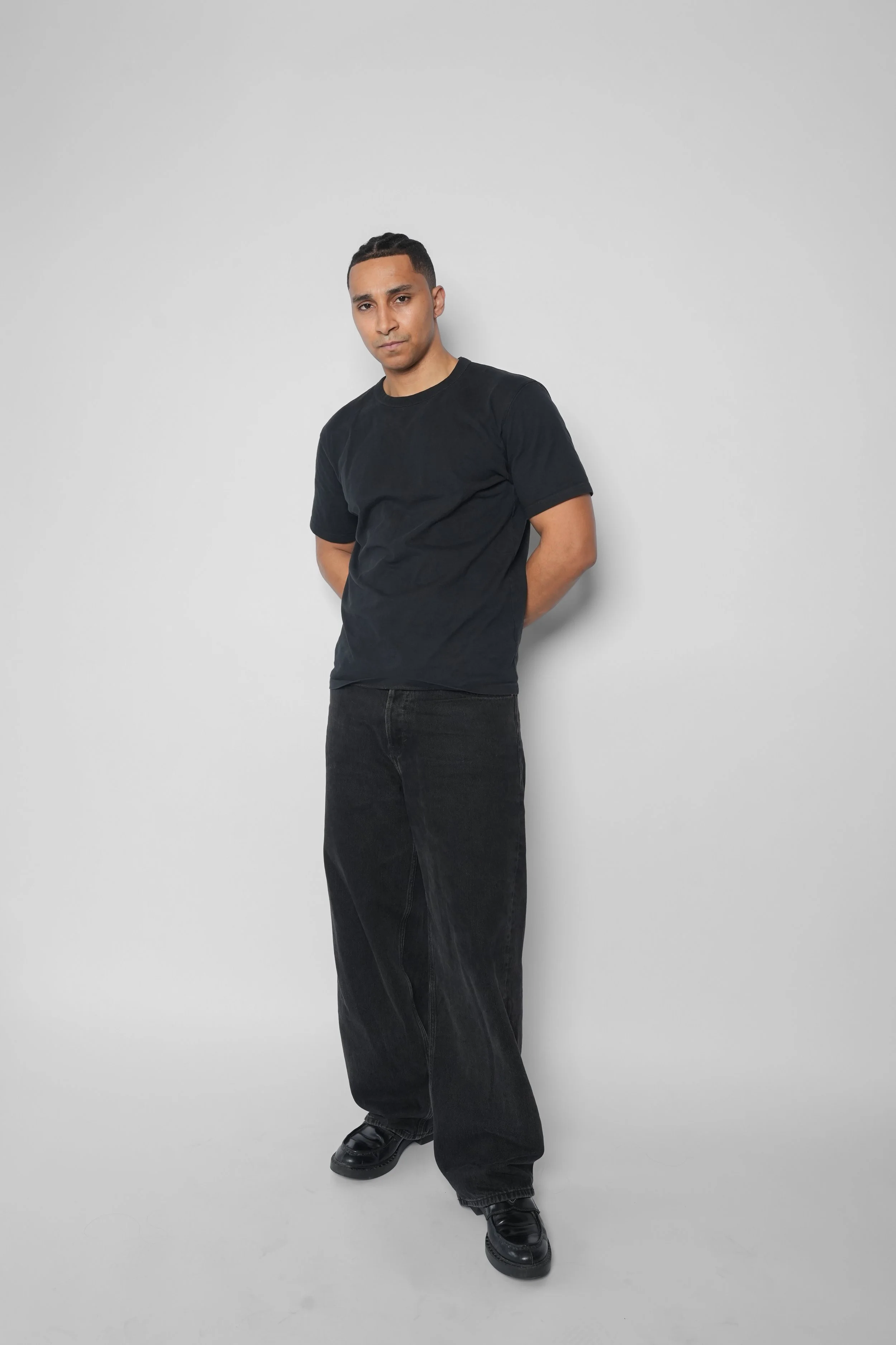 Mand i sort t-shirt og bukser står mod en hvid væg.