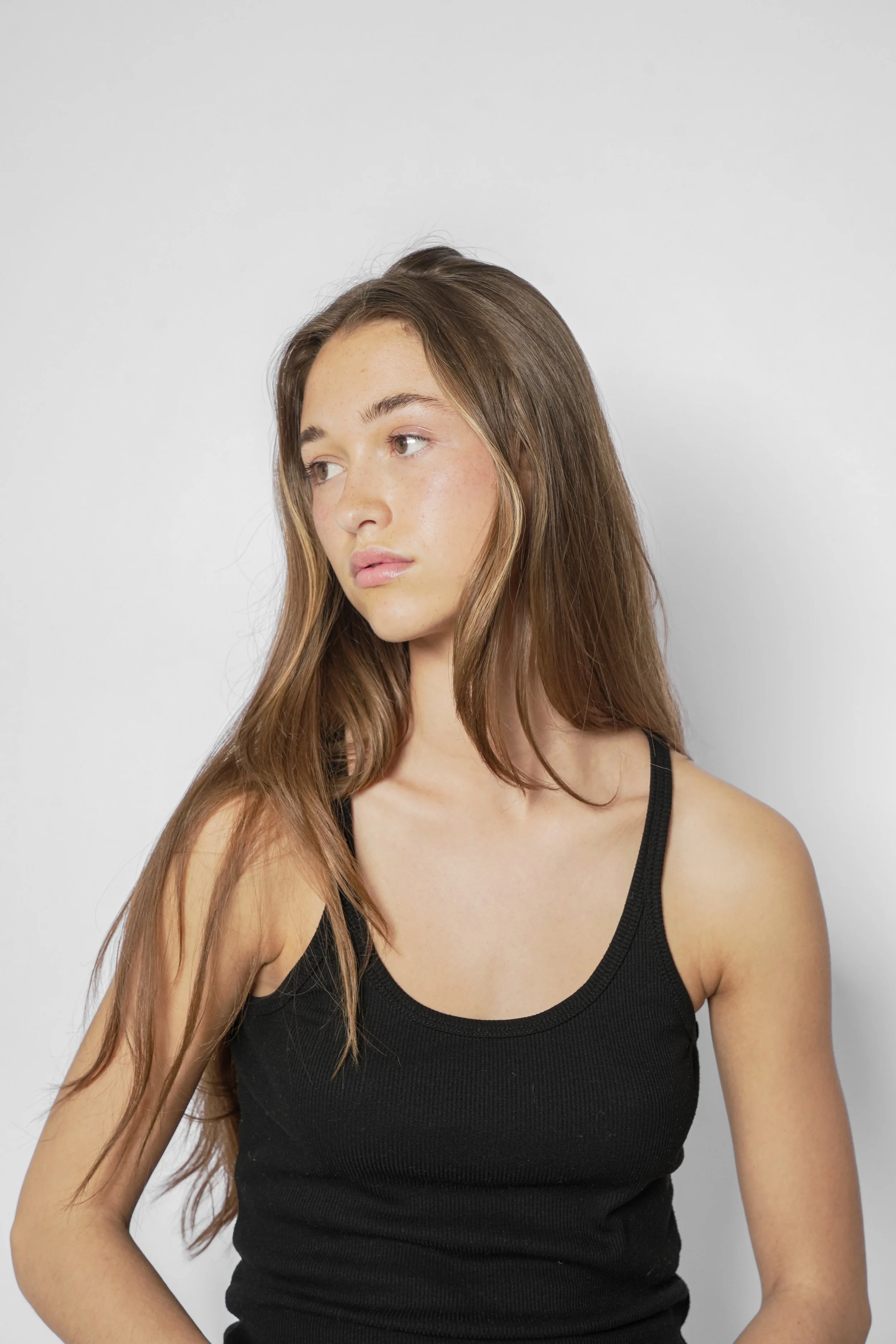 En ung kvinde med langt brunt hår, iført sort tanktop, ser væk med neutral ud mod venstre.