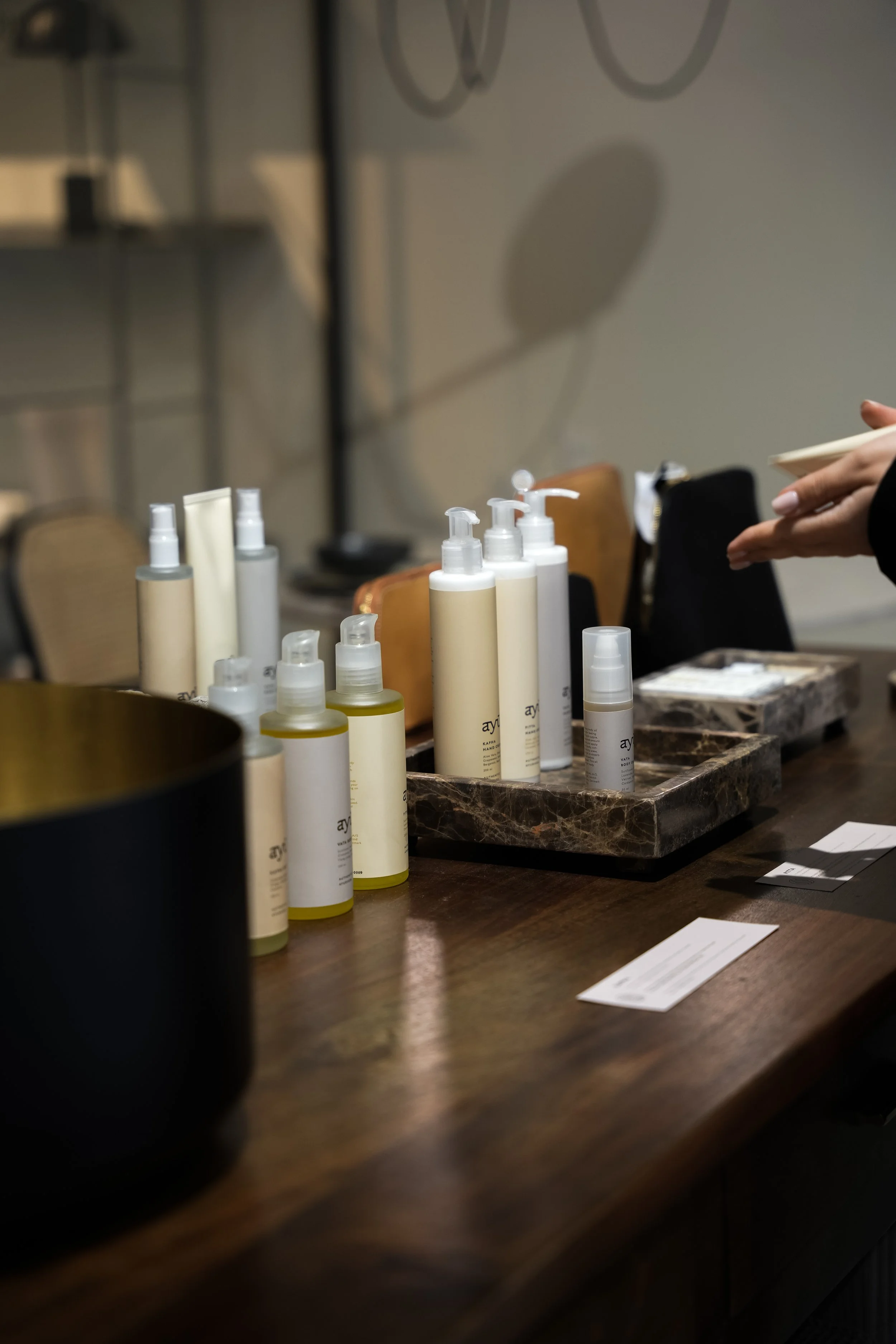Skønhedsprodukter, herunder cremer og sprøjter, arrangeret på en træbord med en person, der håndterer dem i baggrunden.