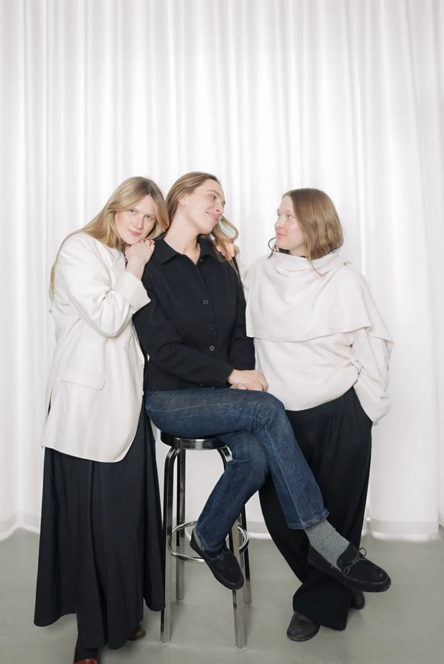 Tre kvinder, der sidder sammen foran en hvid curtain, smiler og har en venlig samtale.