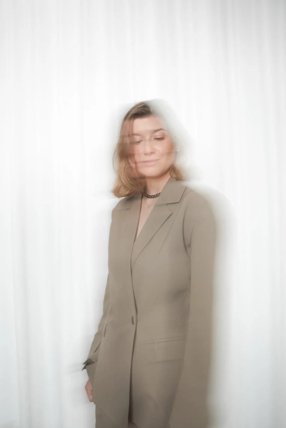 Kvinde i grådragt stående foran en lys baggrund med en sløret effekt omkring hende.