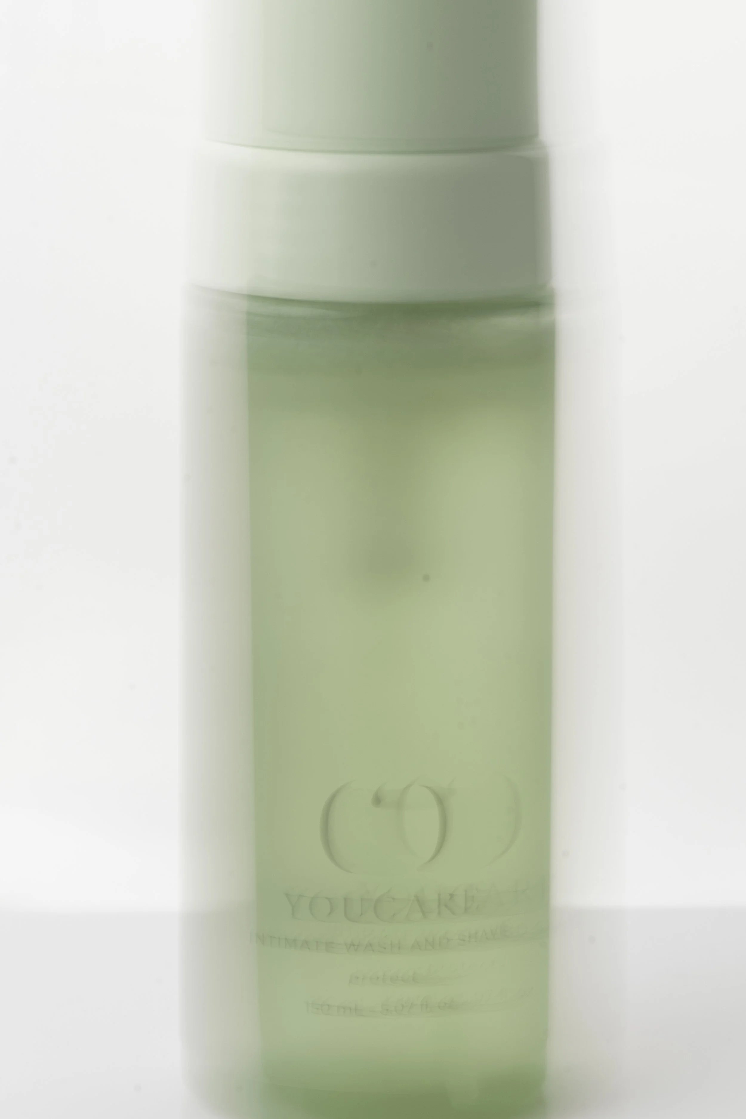 En grøn flaske med mærket 'YOUCARE' på, står mod en lys baggrund.