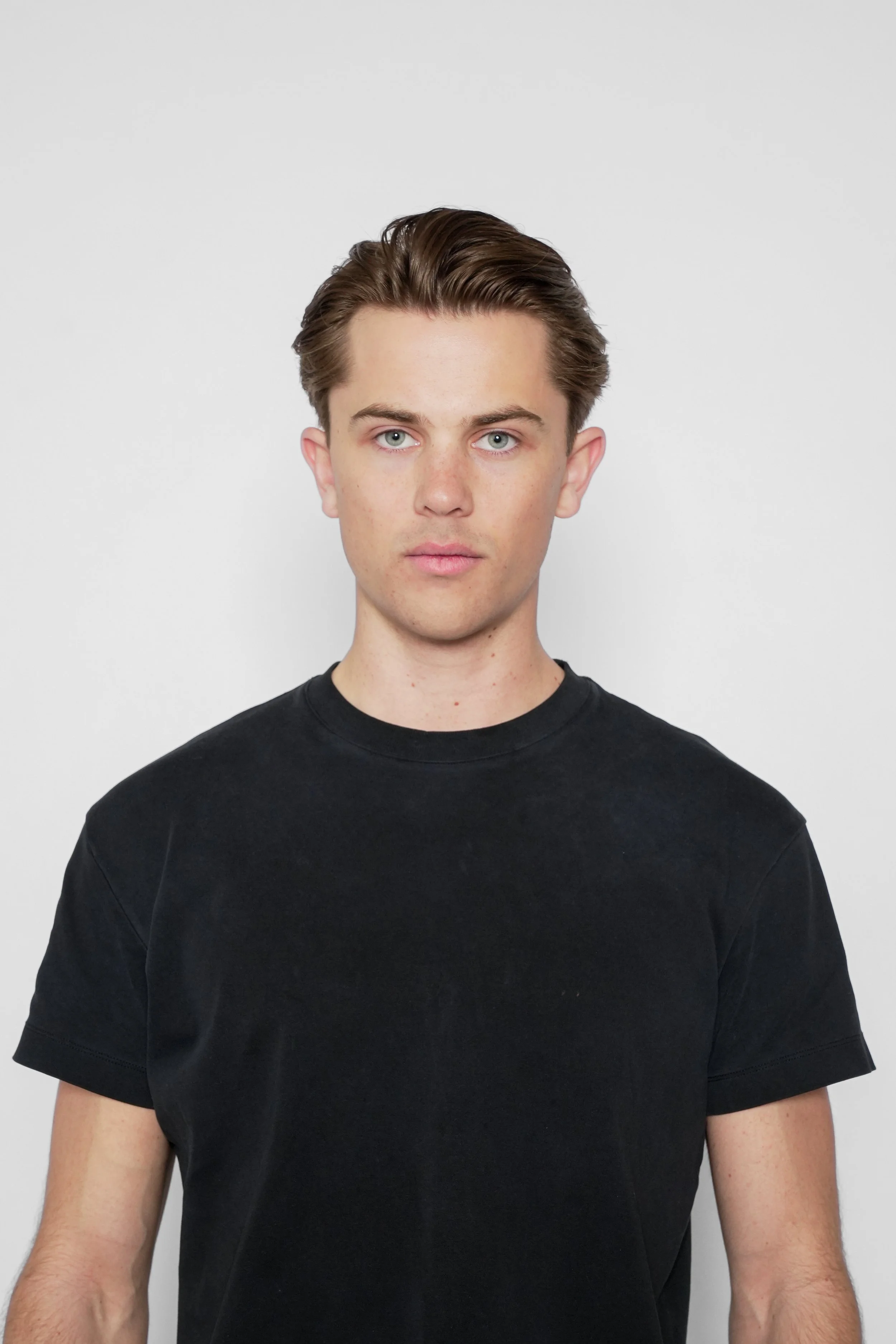 Ung mand i sort T-shirt med lyst hår og blå øjne mod en hvid baggrund