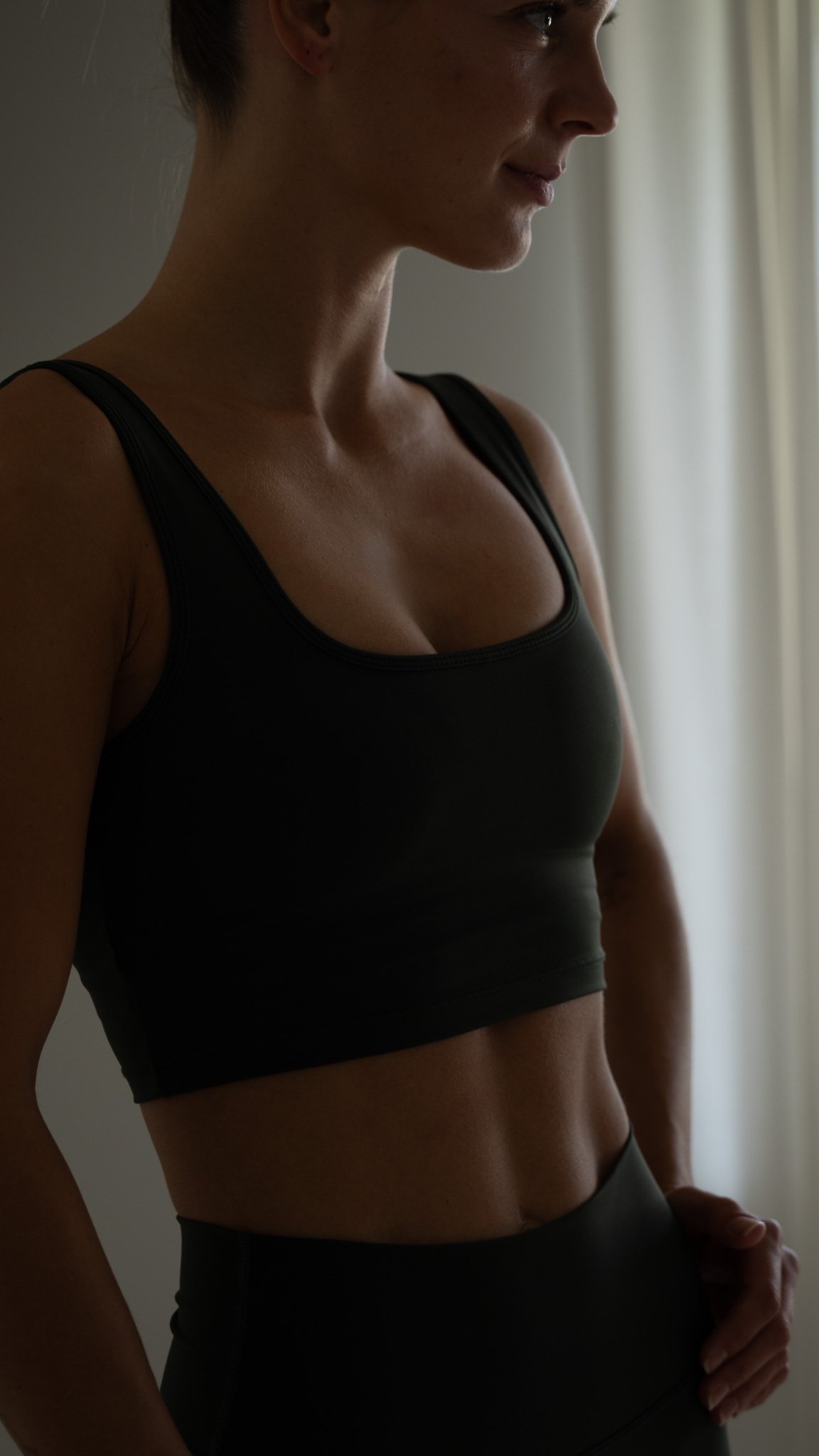 Kvinde i træningstøj står ved siden af et vindue, set i profil.