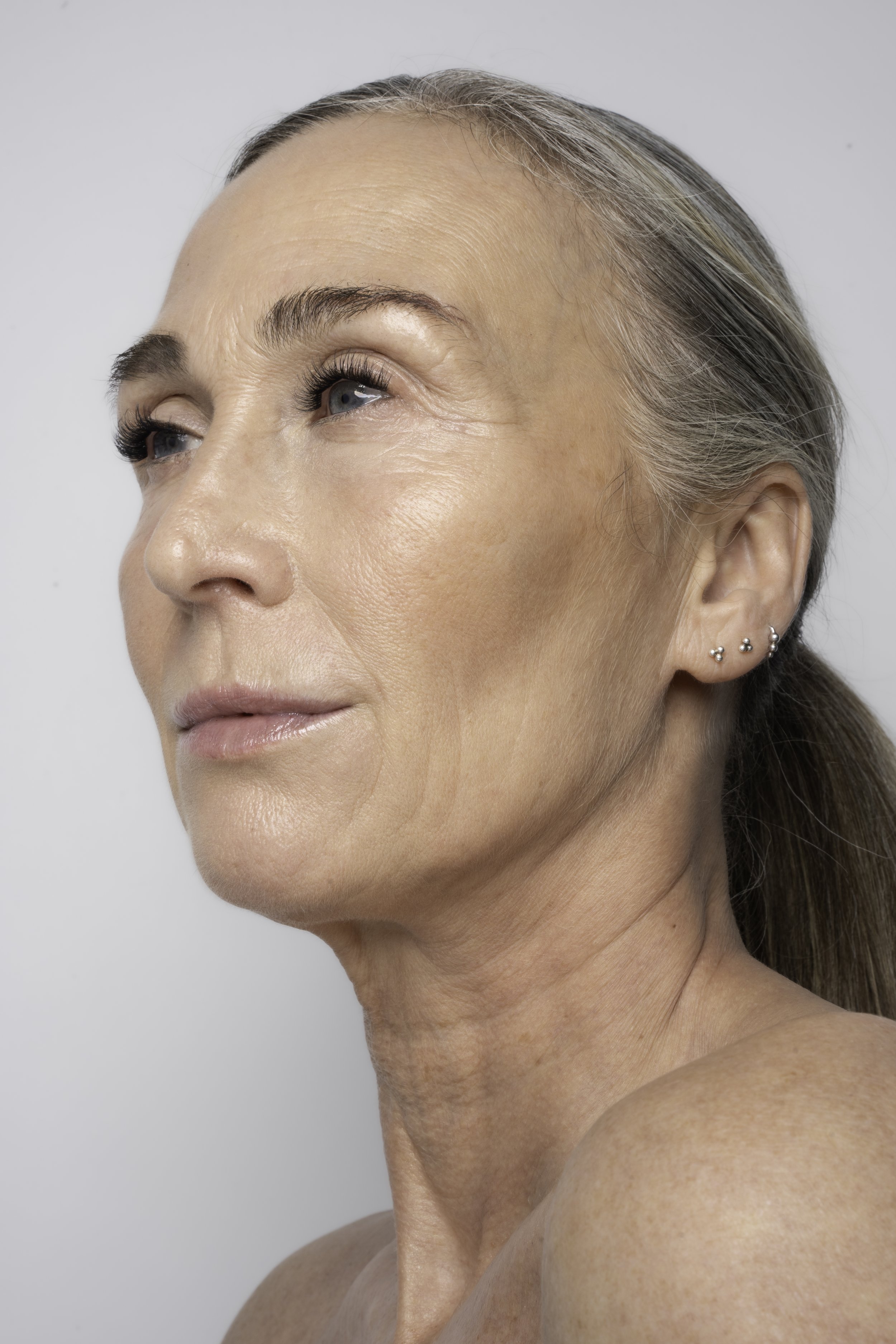 Portræt af en ældre kvinde med grå hår, der kigger let til siden, mod en lys baggrund.