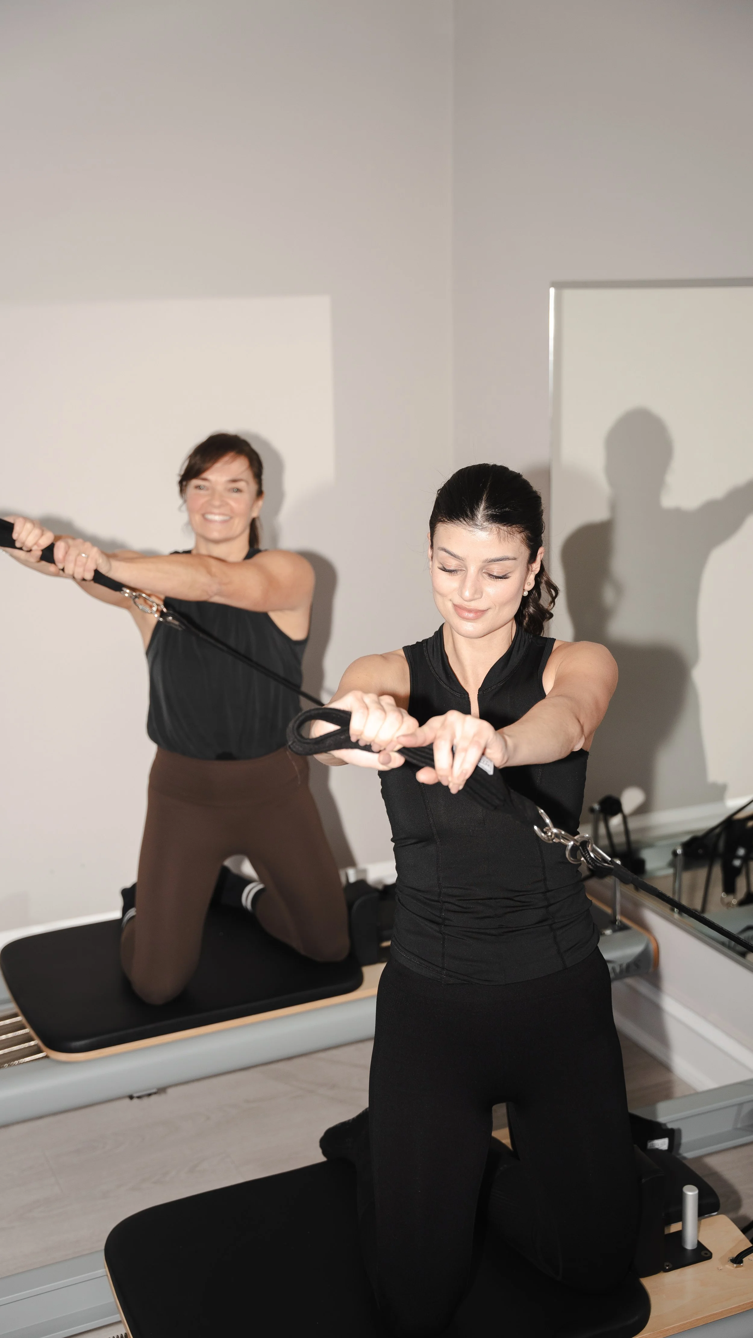 To kvinder træner styrketræning på en reformer i et træningslokale.