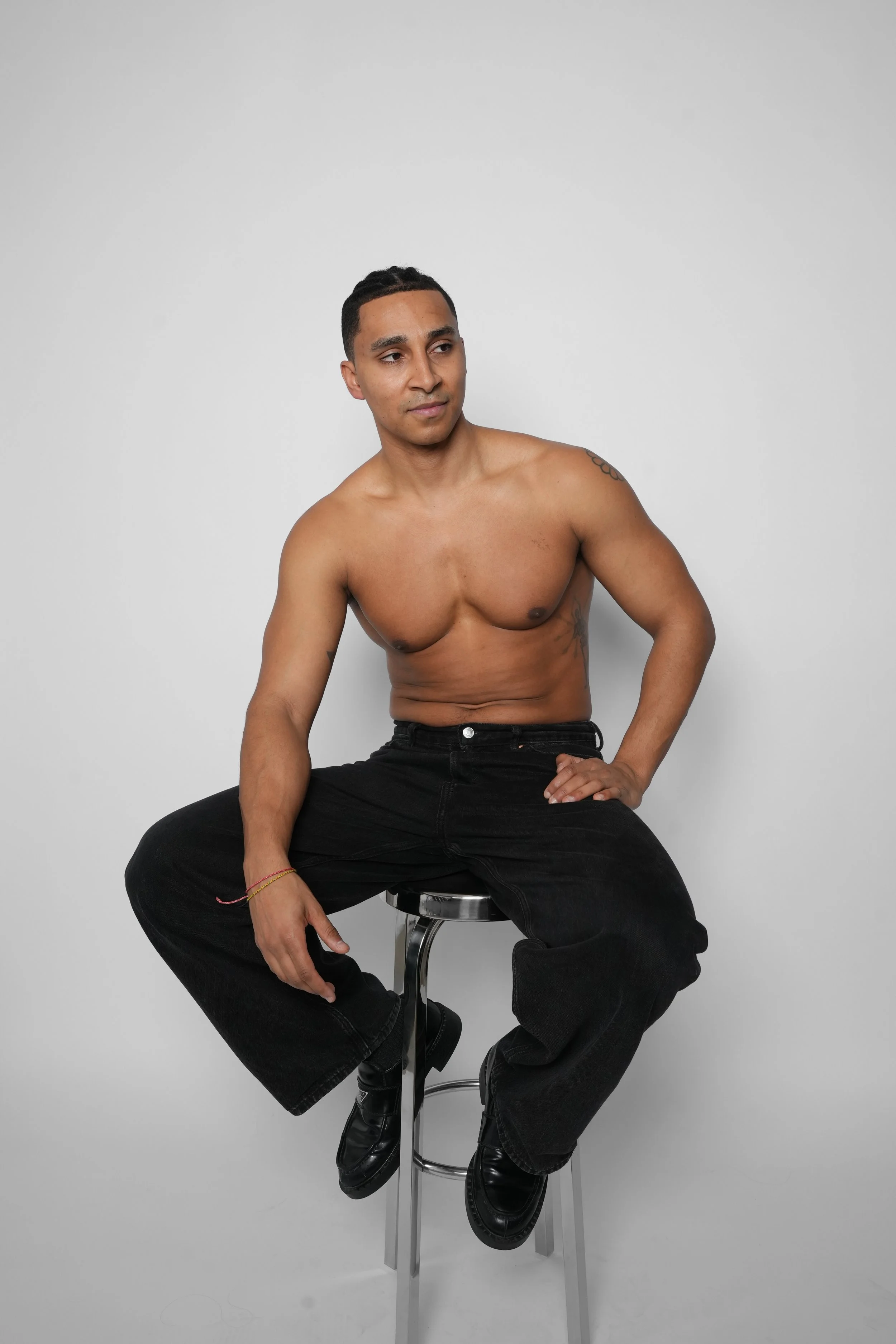 Ung mand sidder på en barstol uden tøj over brystet mod en hvid baggrund.