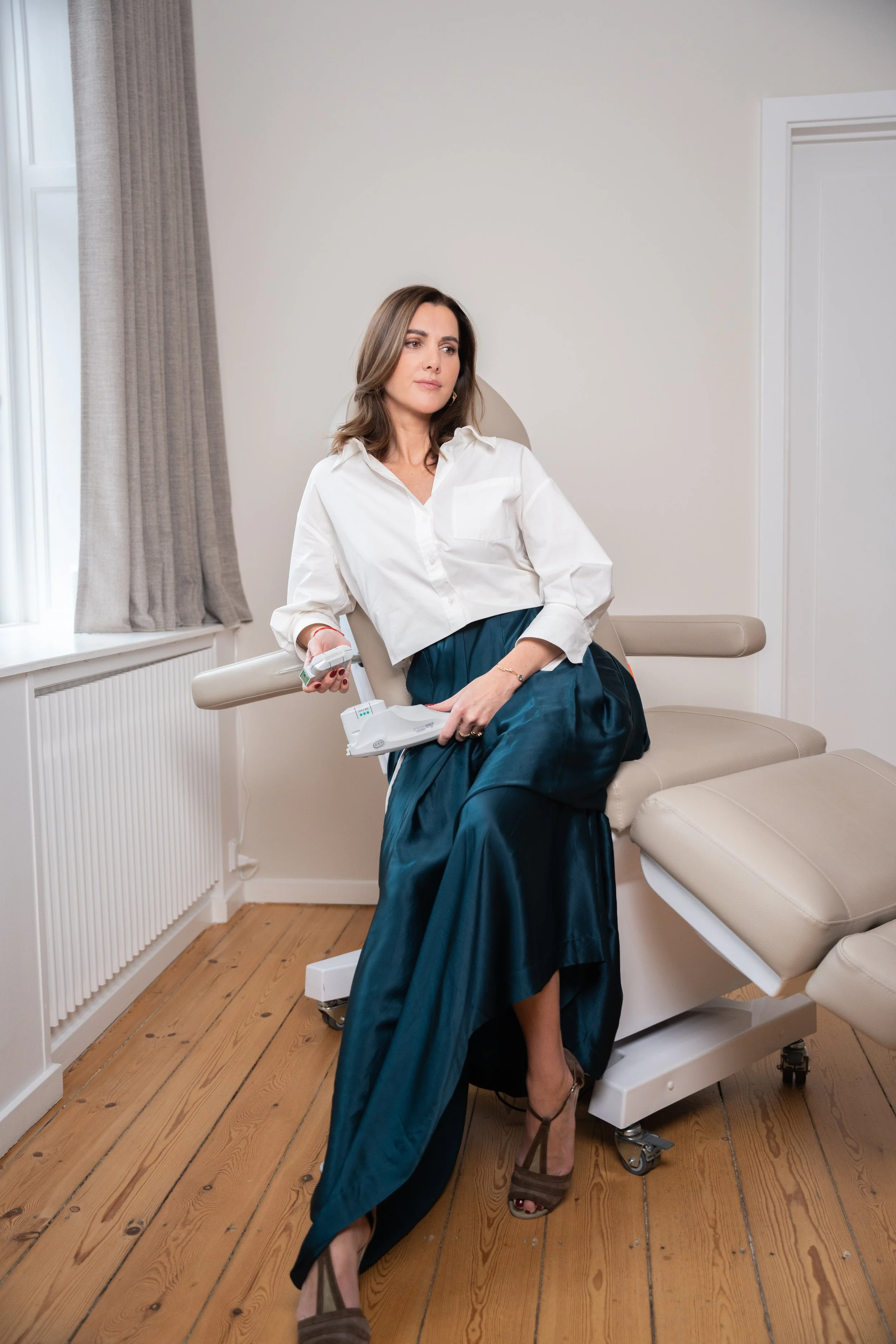 Kvinde sidder iført en hvid skjorte og en lang, blå nederdel, mens hun holder en medicinsk enhed i hånden.