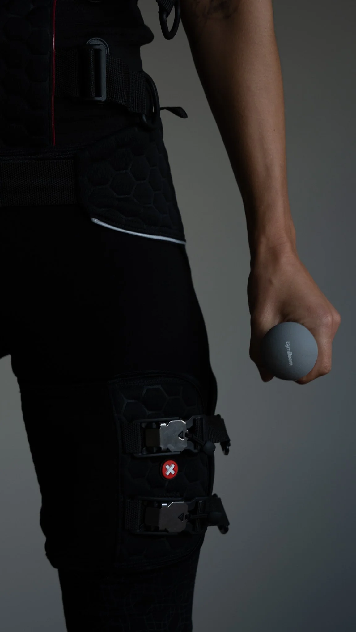 En person iført sort sportsudstyr, der holder en grå træningsvægt i hånden. 