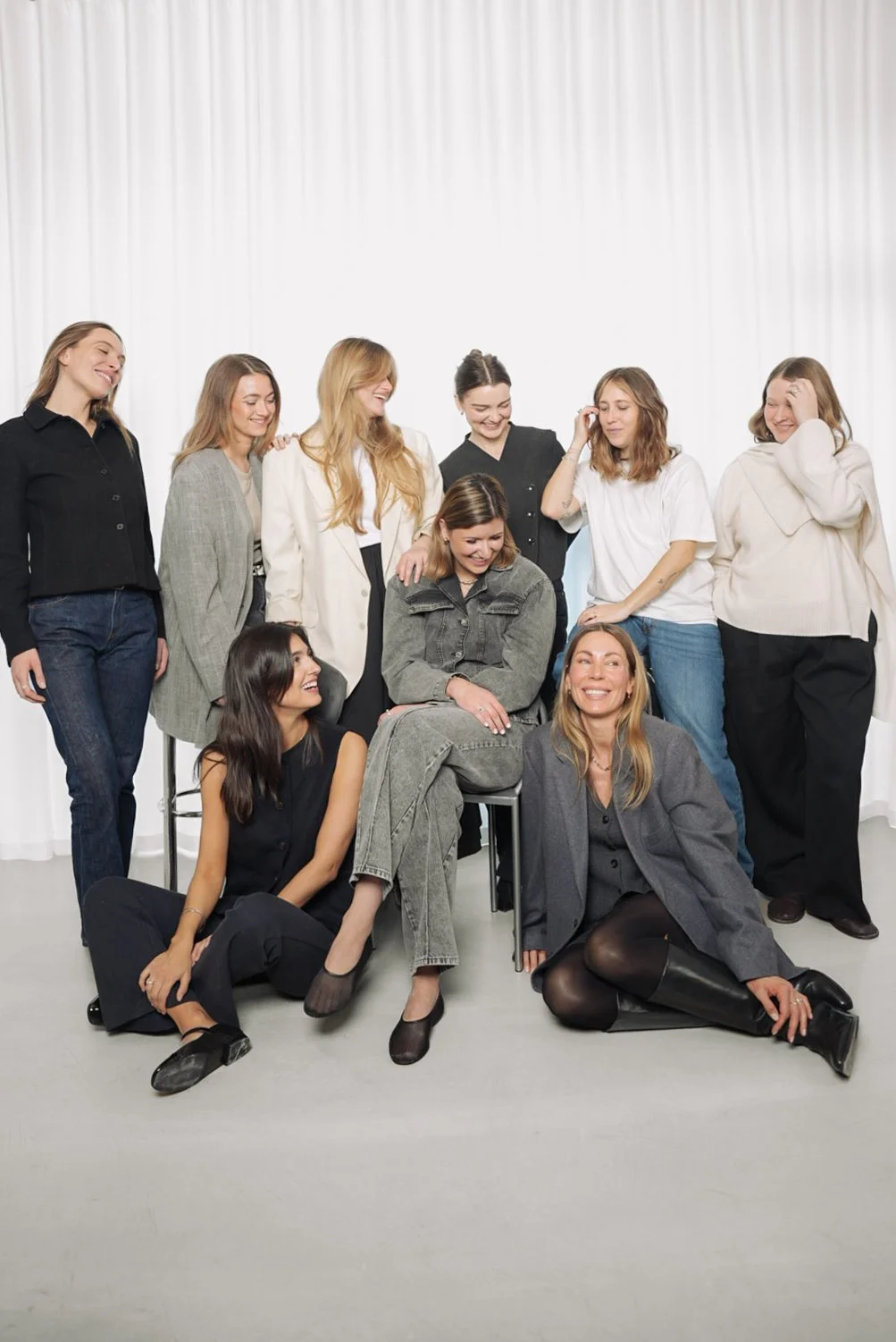 En gruppe kvinder står og sidder sammen foran en hvid baggrund, alle smiling og har en god stemning.