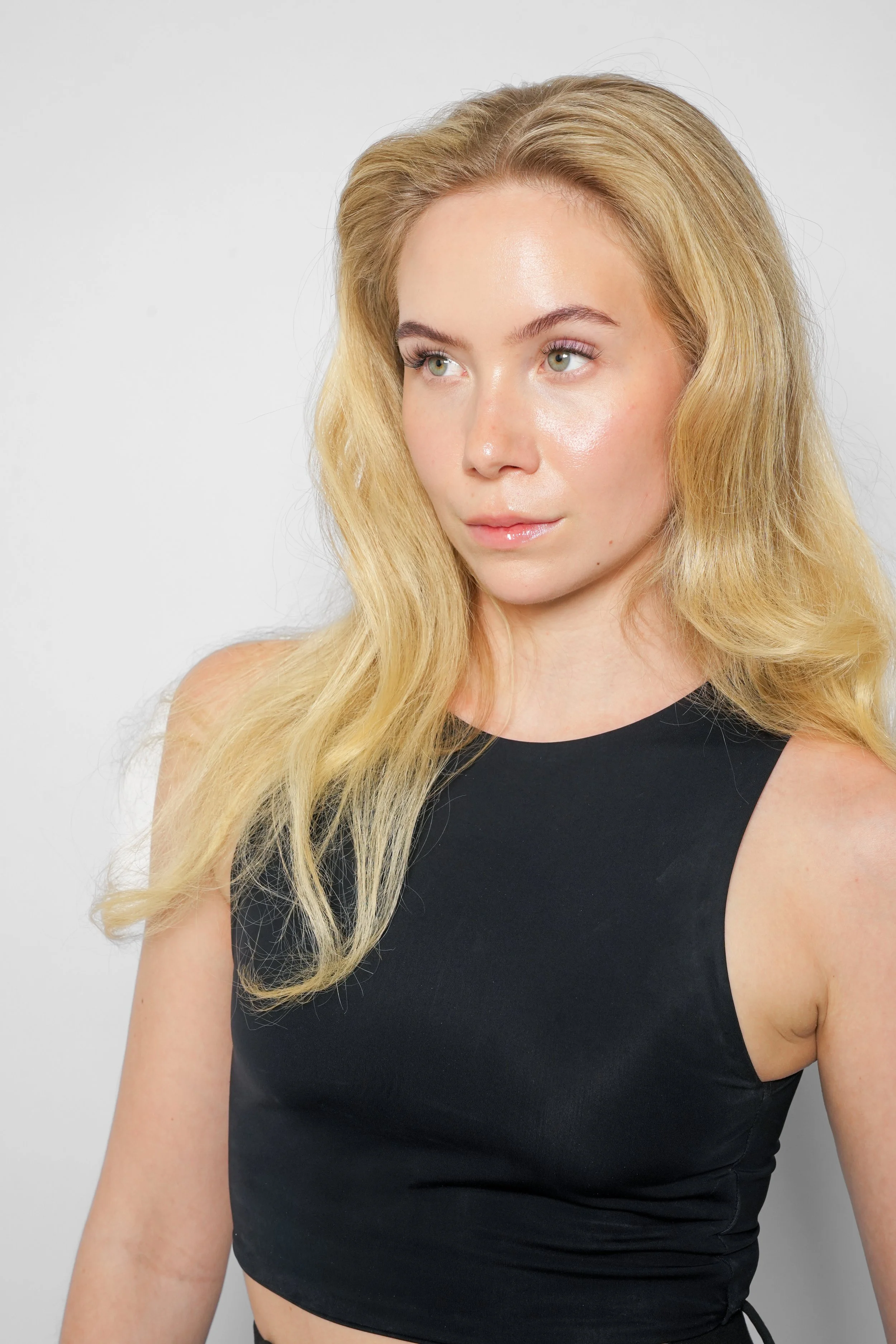Et portræt af en ung kvinde med blond, bølget hår iført en sort top mod en hvid baggrund.