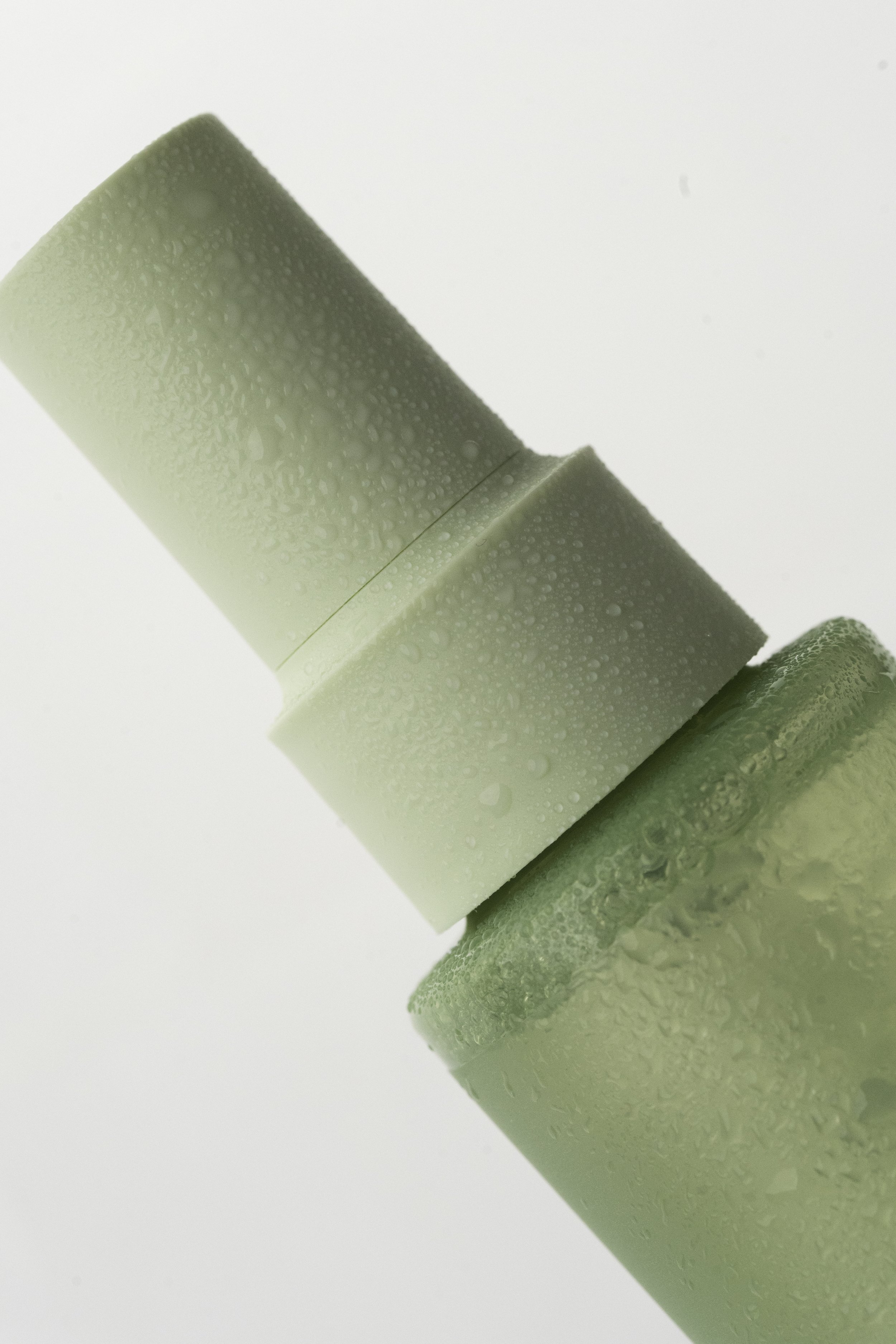 To grønne skumruller med vanddropletter, placeret i en lodret vinkel.