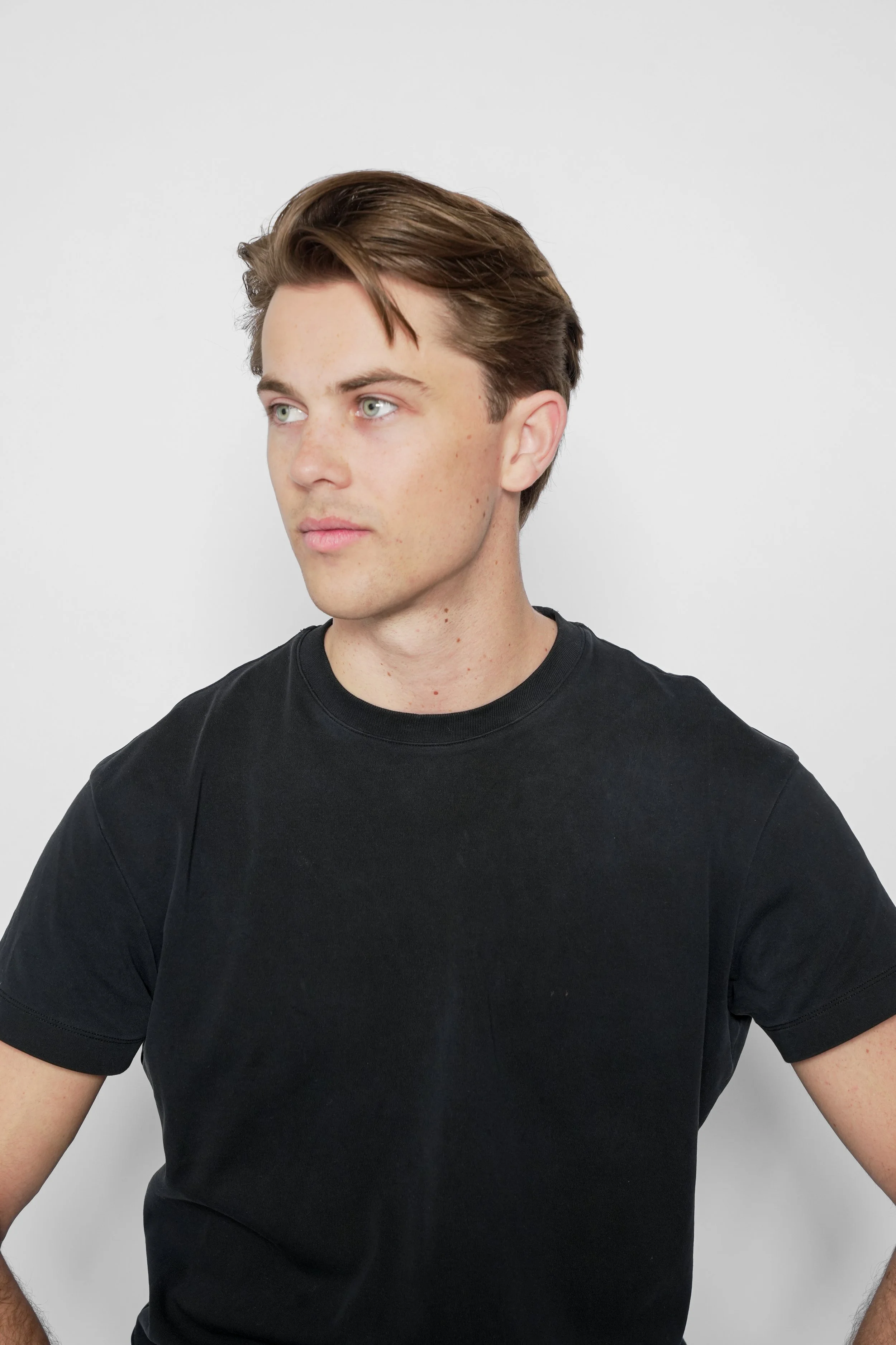 Ung mand med lyst hår og blå øjne, iført sort T-shirt, ser til højre, foran en lys grå baggrund.