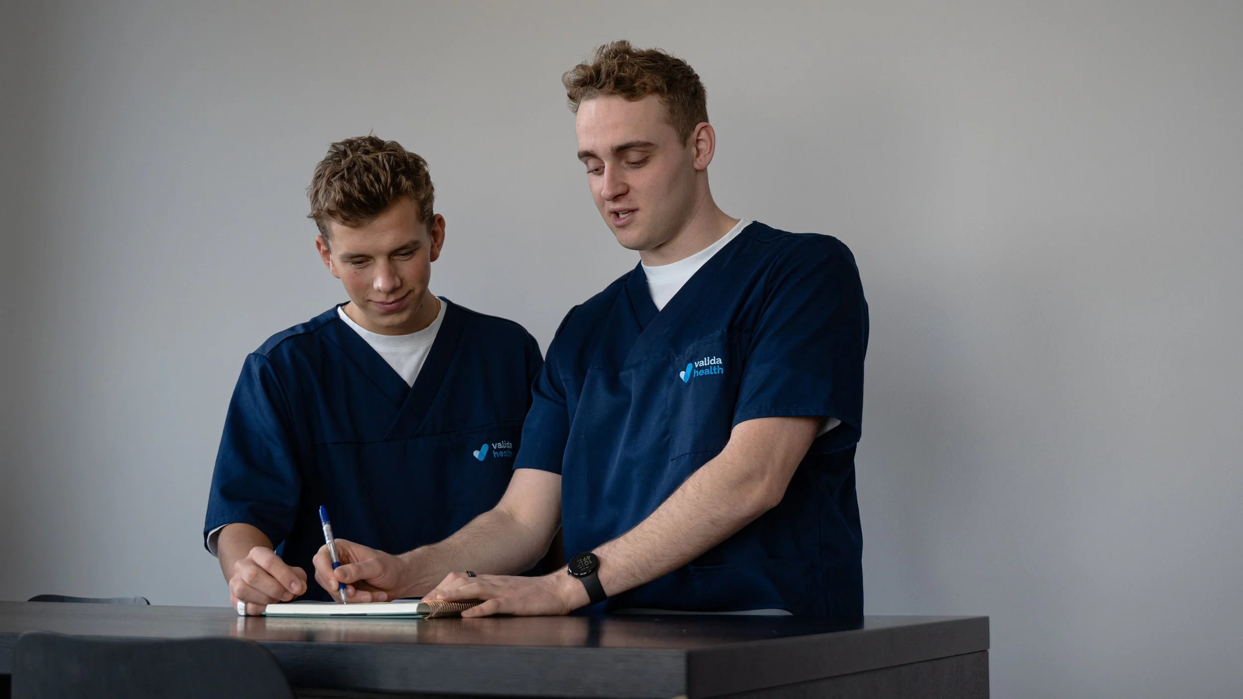 To unge mænd i blå uniformer skriver i en notesbog på et skrivebord.